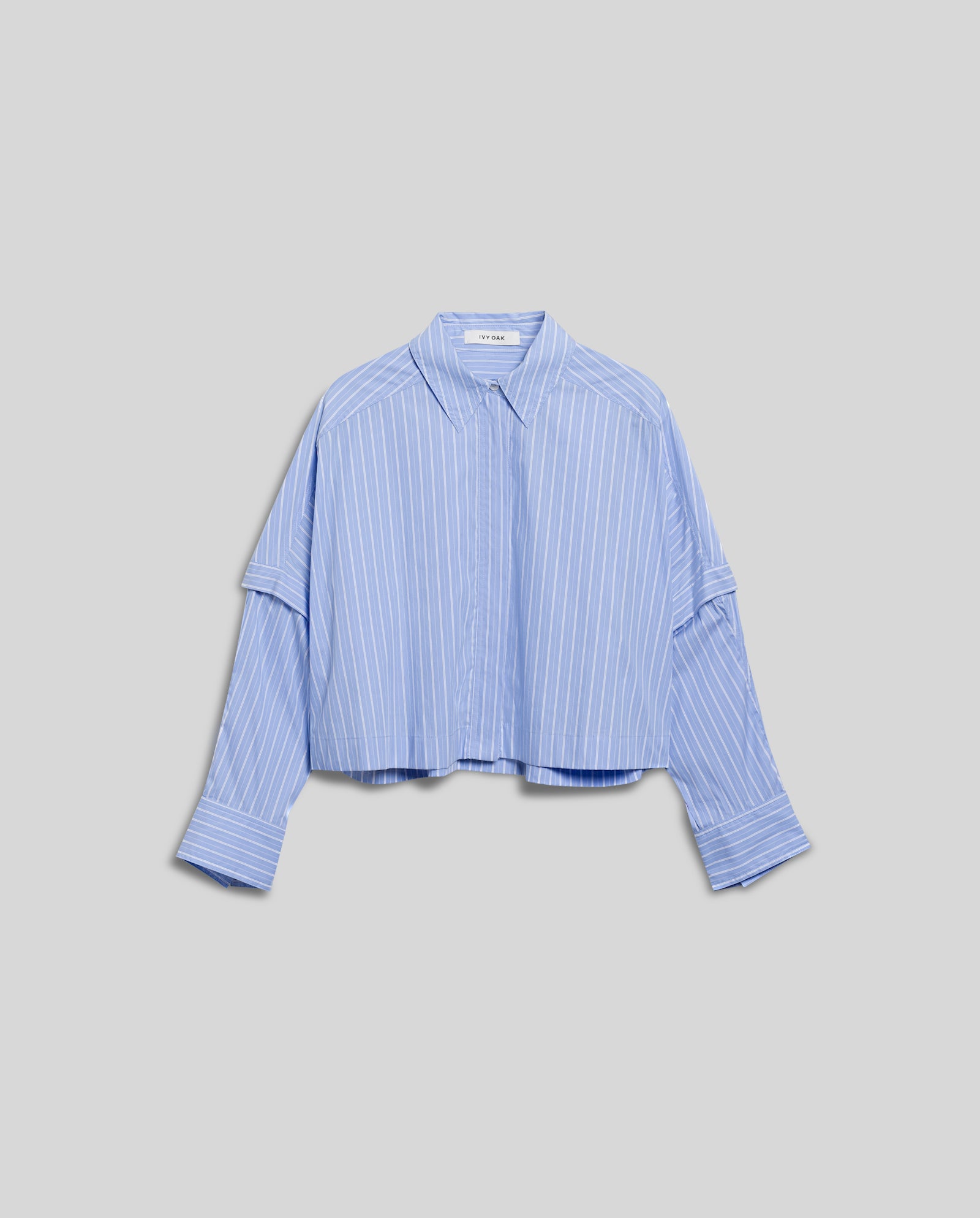 The IVY OAK ELVIRA Blouse is light blue with white vertical stripes, features long detachable sleeves and a cropped button-up style, shown on a gray background.