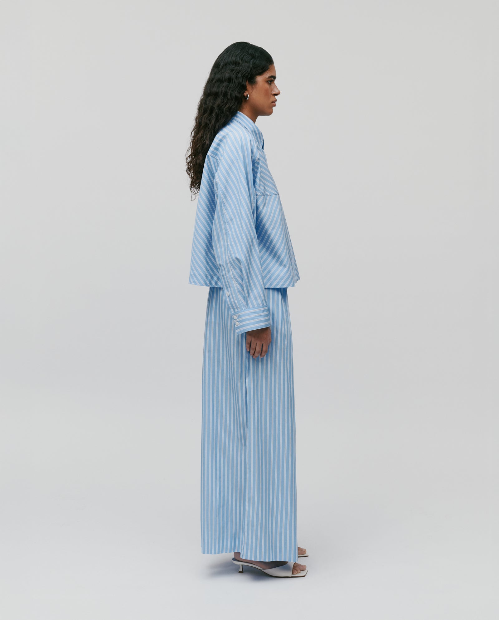 A person wears the IVY OAK BRITTNEY Blouse in light blue and white with a boxy fit, standing sideways against a plain light background.