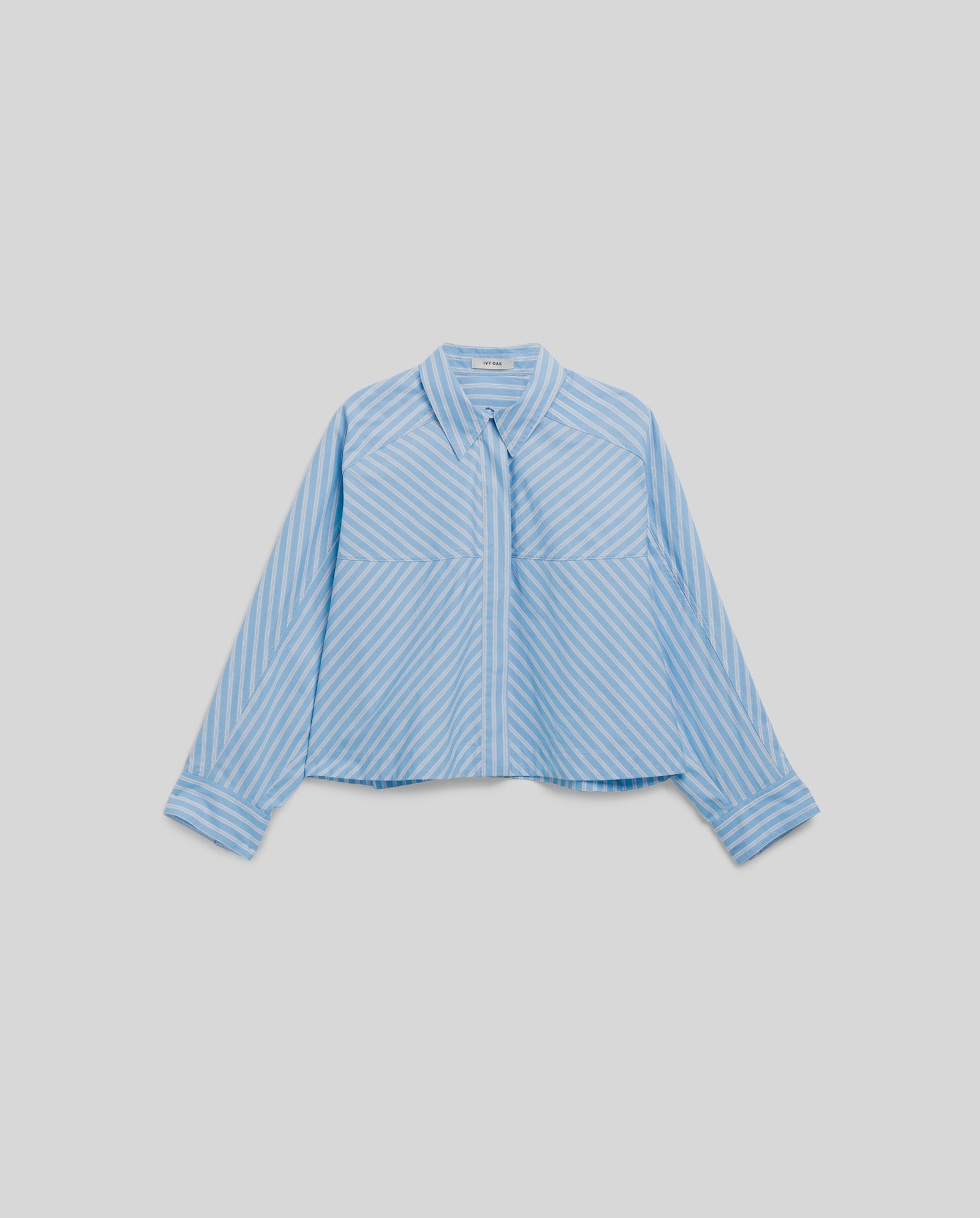 The IVY OAK BRITTNEY Blouse features light blue and white stripes, long sleeves, a collar, and a boxy fit, displayed on a plain background.