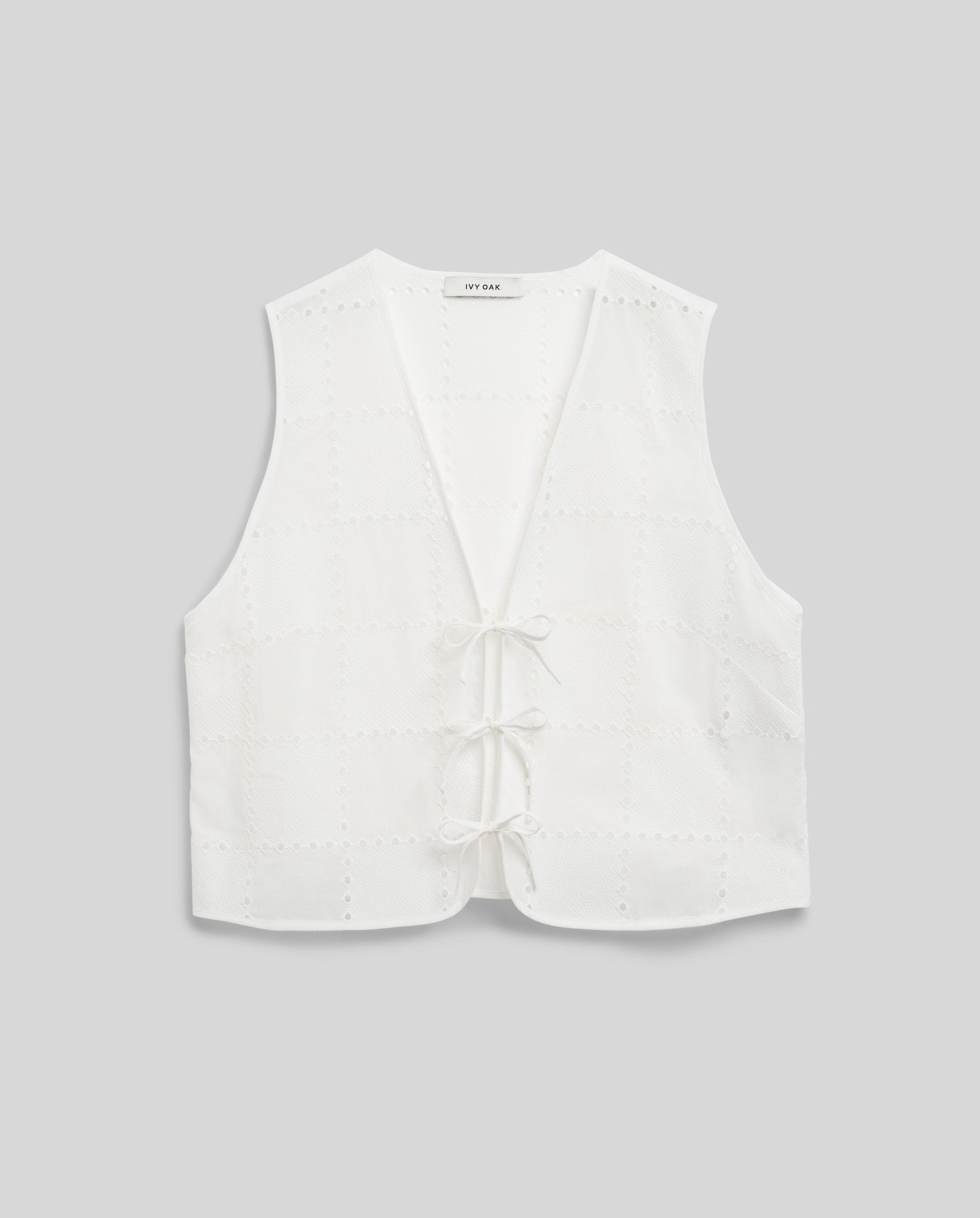 White sleeveless IVY OAK TALA Top with embroidered anglaise eyelet pattern and front tie closures, shown on a plain gray background.