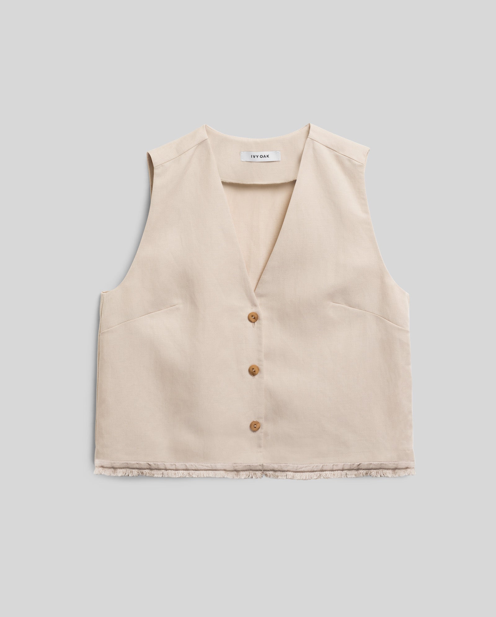 The TALA ANN Top by IVY OAK is a sleeveless beige vest with a V-neckline and three brown buttons, made from a soft linen blend and shown against a plain gray background.