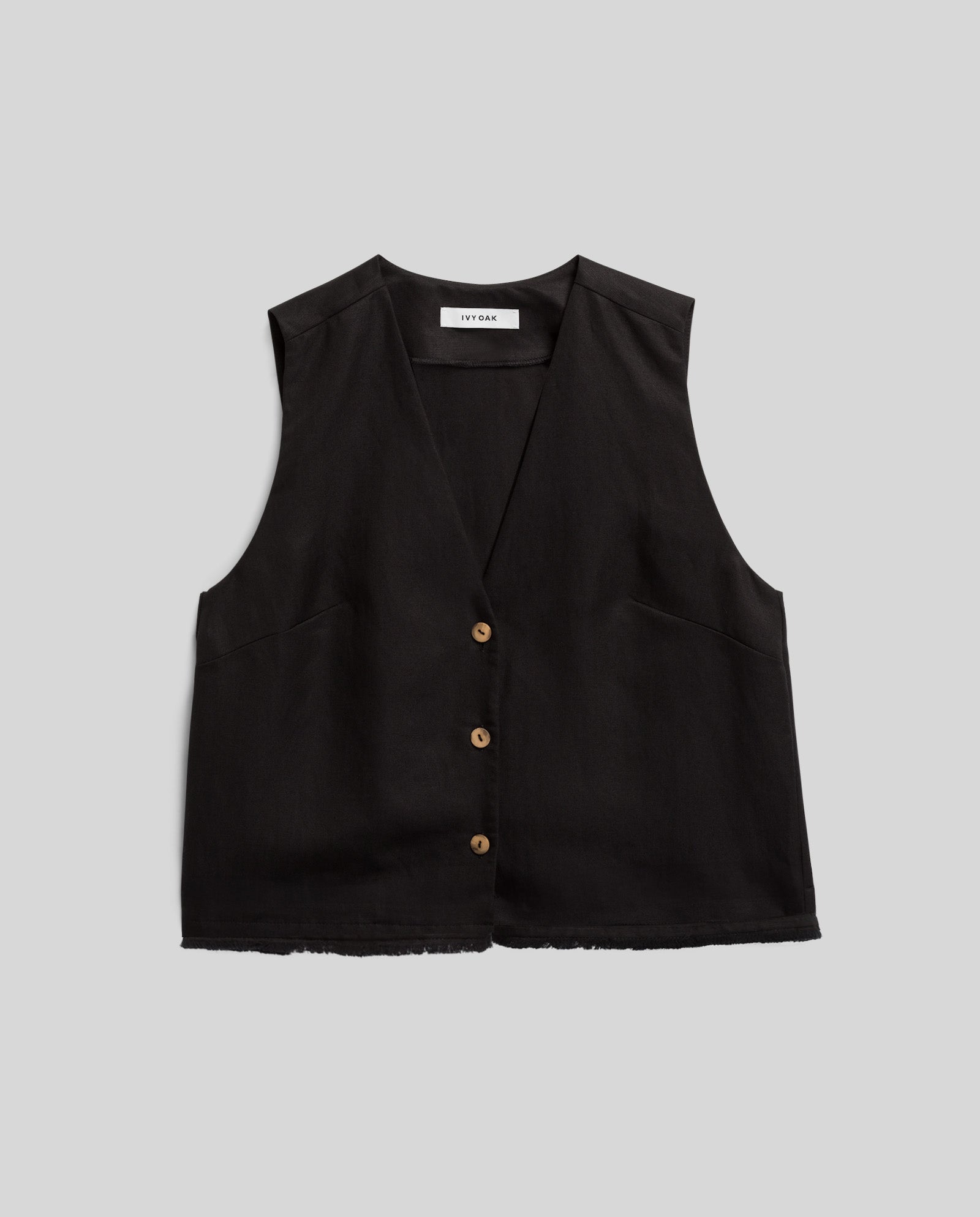 The TALA ANN Top by IVY OAK is a sleeveless black vest featuring three brown buttons, a V-neckline, raw hem, and subtle fringes, shown against a gray background.