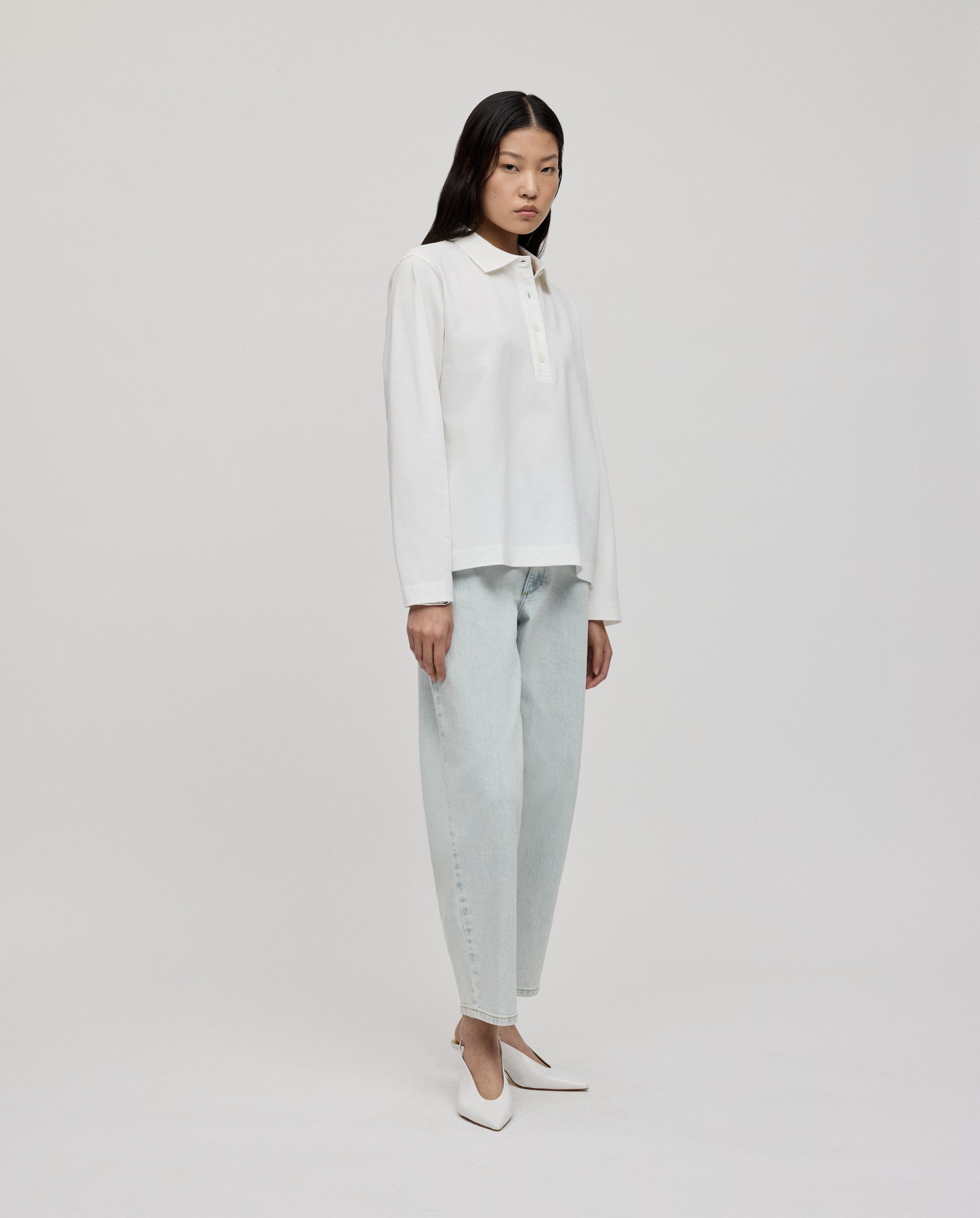 A woman wears the IVY OAK FABIOLA ANN organic cotton long-sleeve polo shirt, styled with light-wash jeans and white heels against a plain background.
