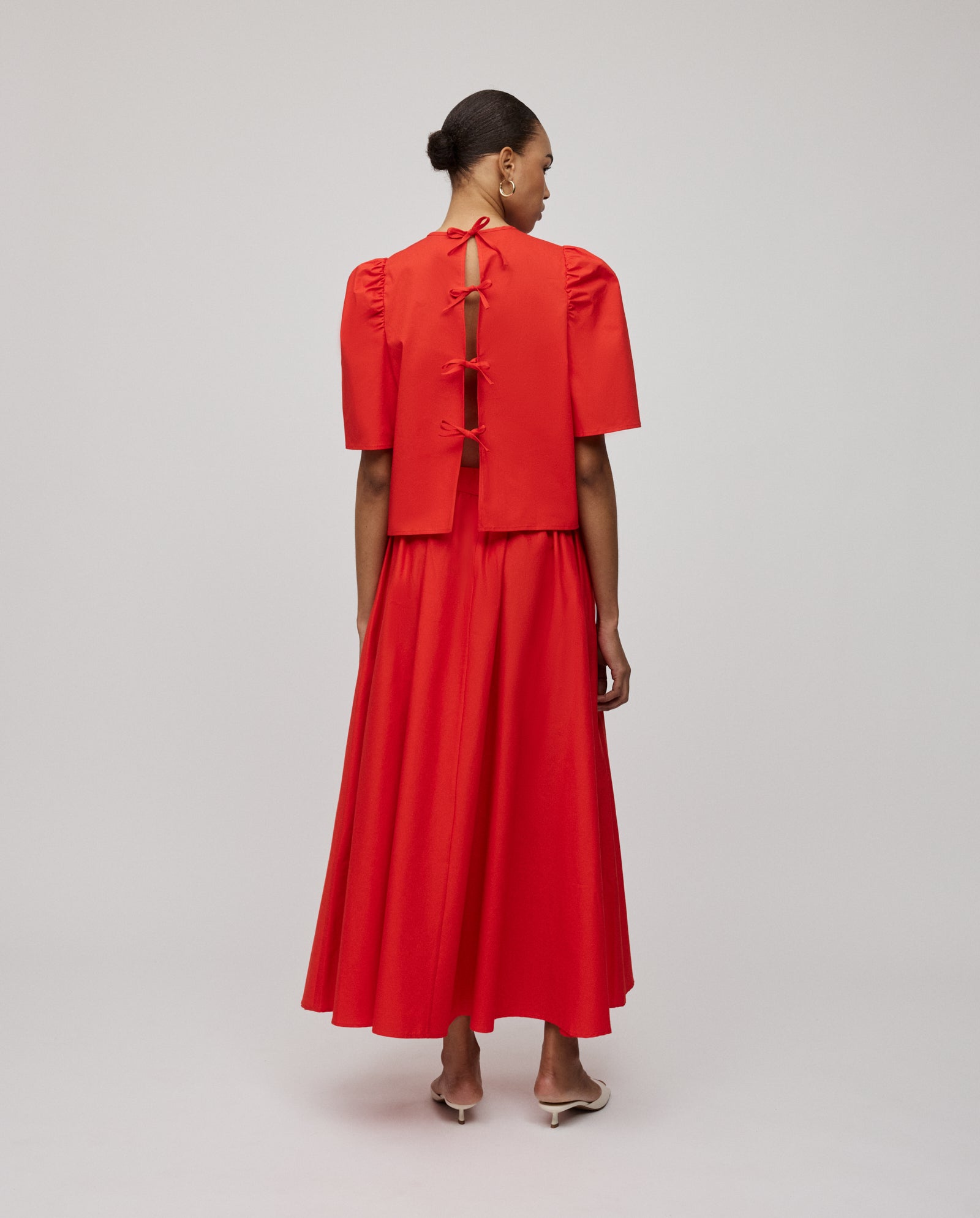 Woman wearing the IVY OAK ELISABETH ANN Blouse in red, featuring voluminous sleeves and bows along the open back, standing with her back to the camera.