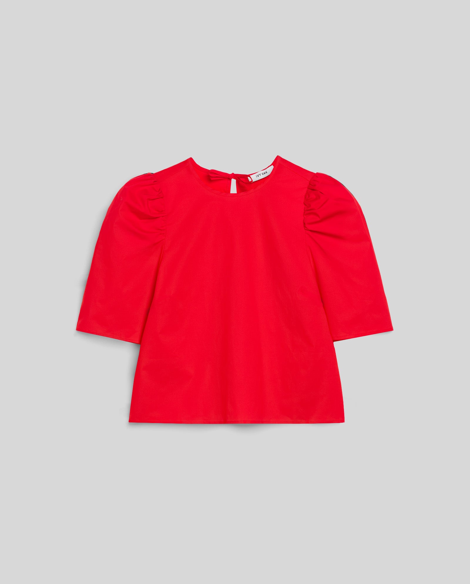 The IVY OAK ELISABETH ANN Blouse is a bright red cropped cotton top with voluminous elbow-length puff sleeves and a keyhole button closure at the back, shown on a gray background.