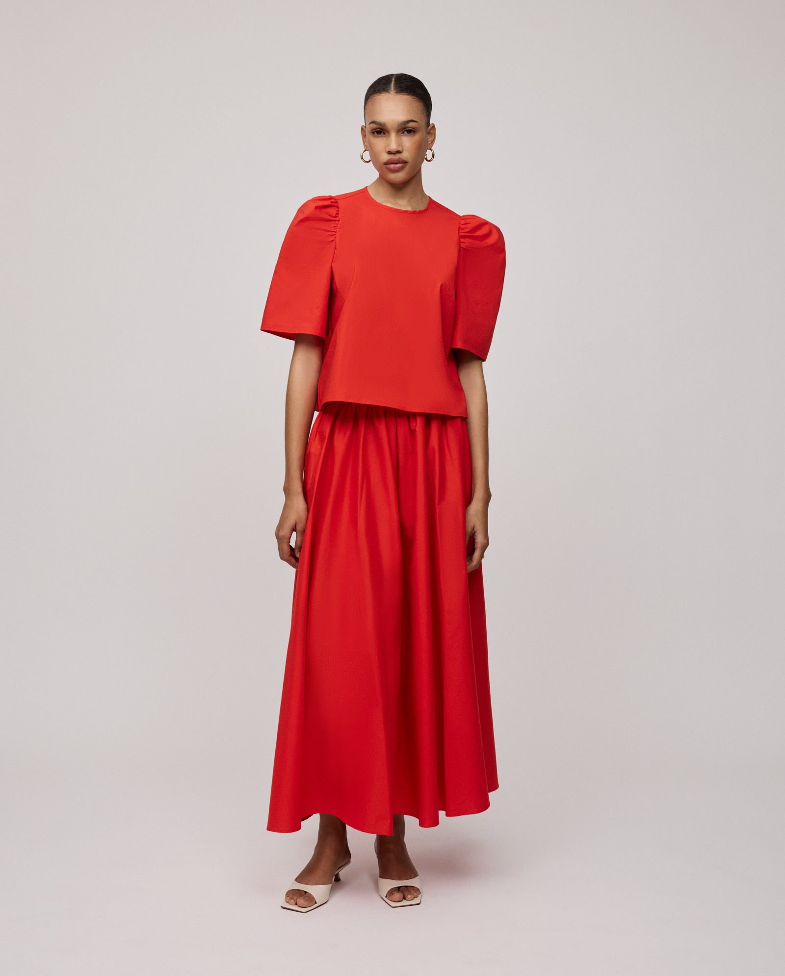 A woman wears the IVY OAK ELISABETH ANN Blouse, featuring voluminous sleeves and a cropped fit, styled with a matching long skirt against a simple light background.