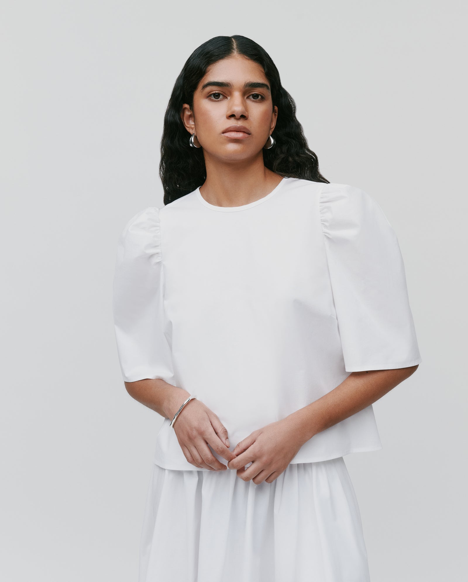 A woman with long dark hair wears the IVY OAK ELISABETH ANN Blouse, featuring voluminous sleeves and a cropped fit, styled with a skirt against a plain background.