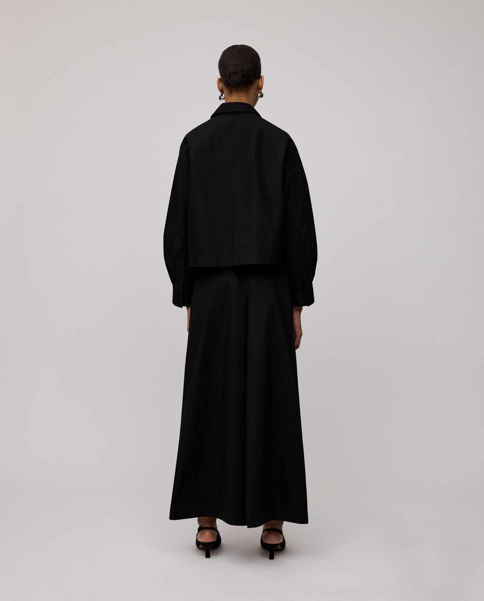 Person with short hair, wearing the IVY OAK BRITTNEY Blouse featuring unique sleeve details and a long black skirt, standing facing away.