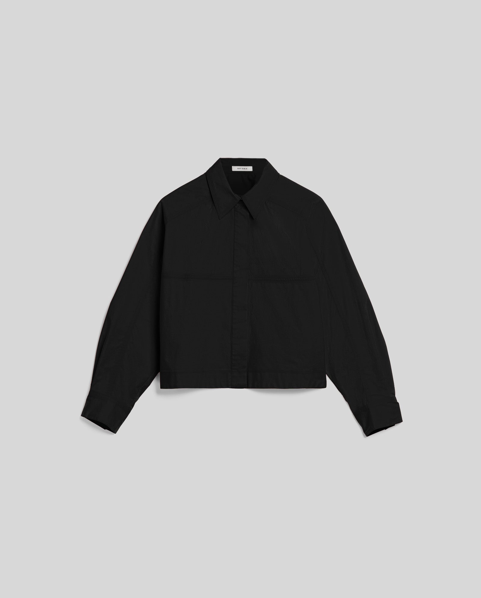 The BRITTNEY Blouse by IVY OAK is a black, boxy shirt blouse with long sleeves, a collared neckline, and unique sleeve detailing, shown against a light gray background.