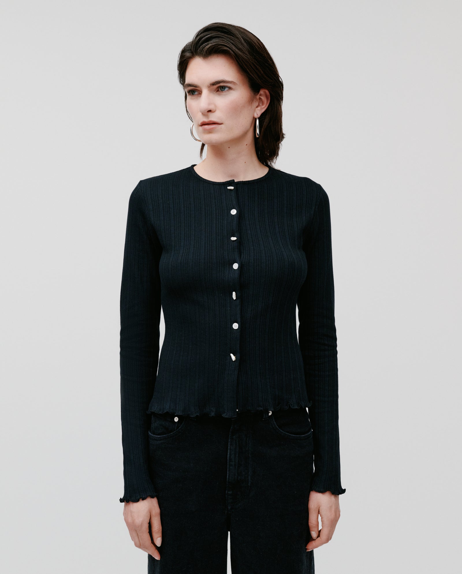 Person wears the IVY OAK KAMILLE black cotton long-sleeve cardigan and black pants, standing against a plain light background.