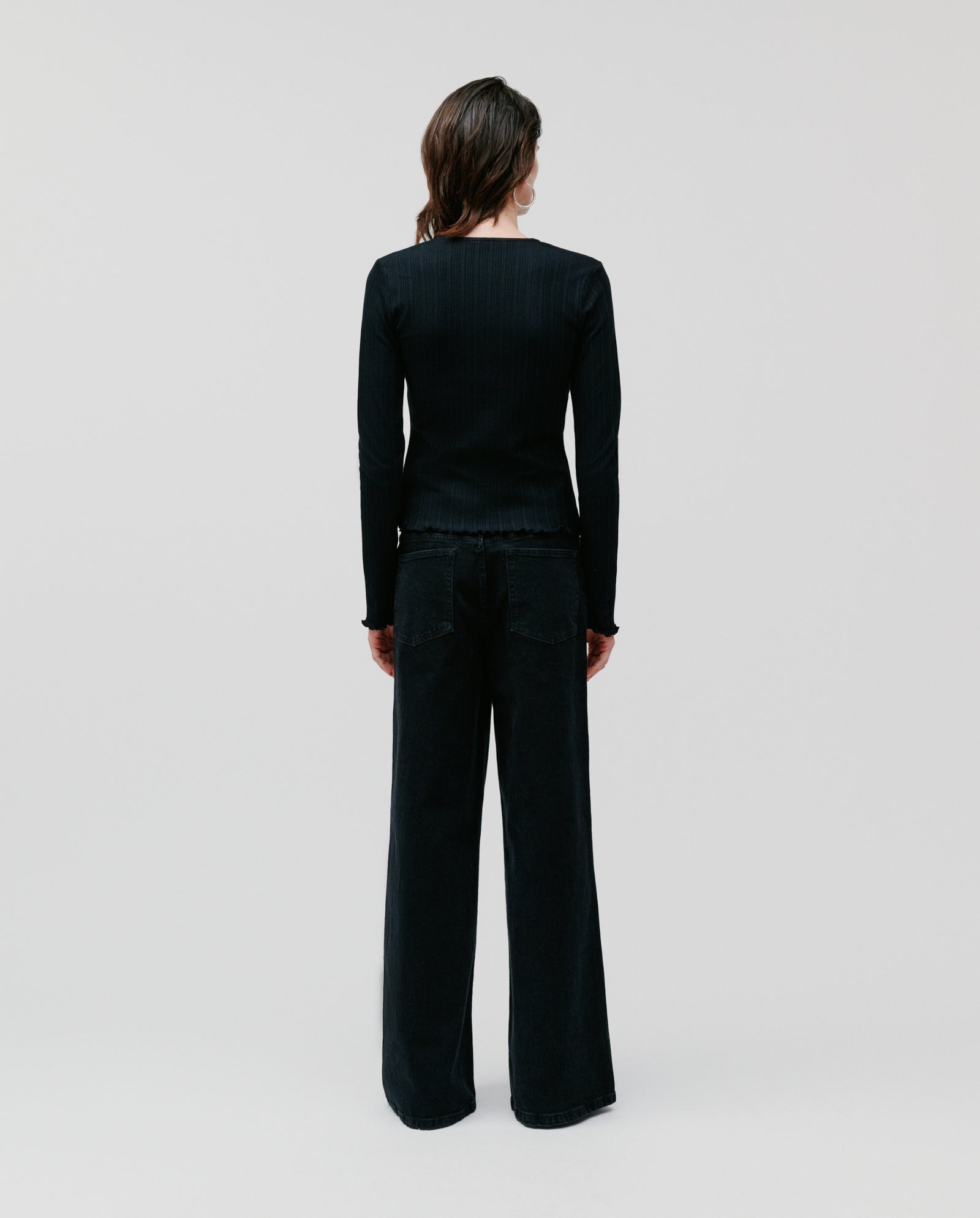 A person stands facing away, dressed in the IVY OAK KAMILLE Cardigan and wide-leg black pants against a plain background.