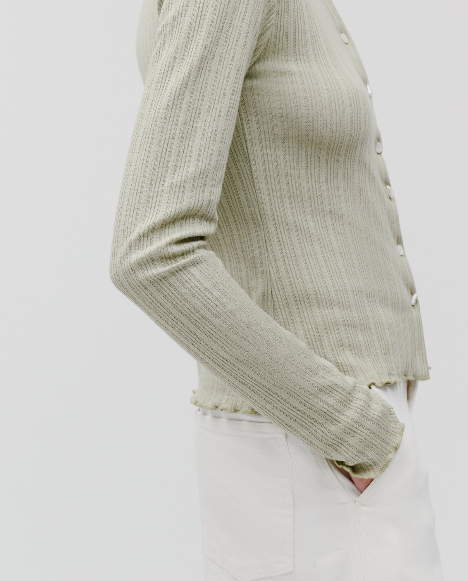 Model wears the IVY OAK KAMILLE Cardigan in light green, classic fit, paired with white pants and hand in pocket, posed against a plain background.