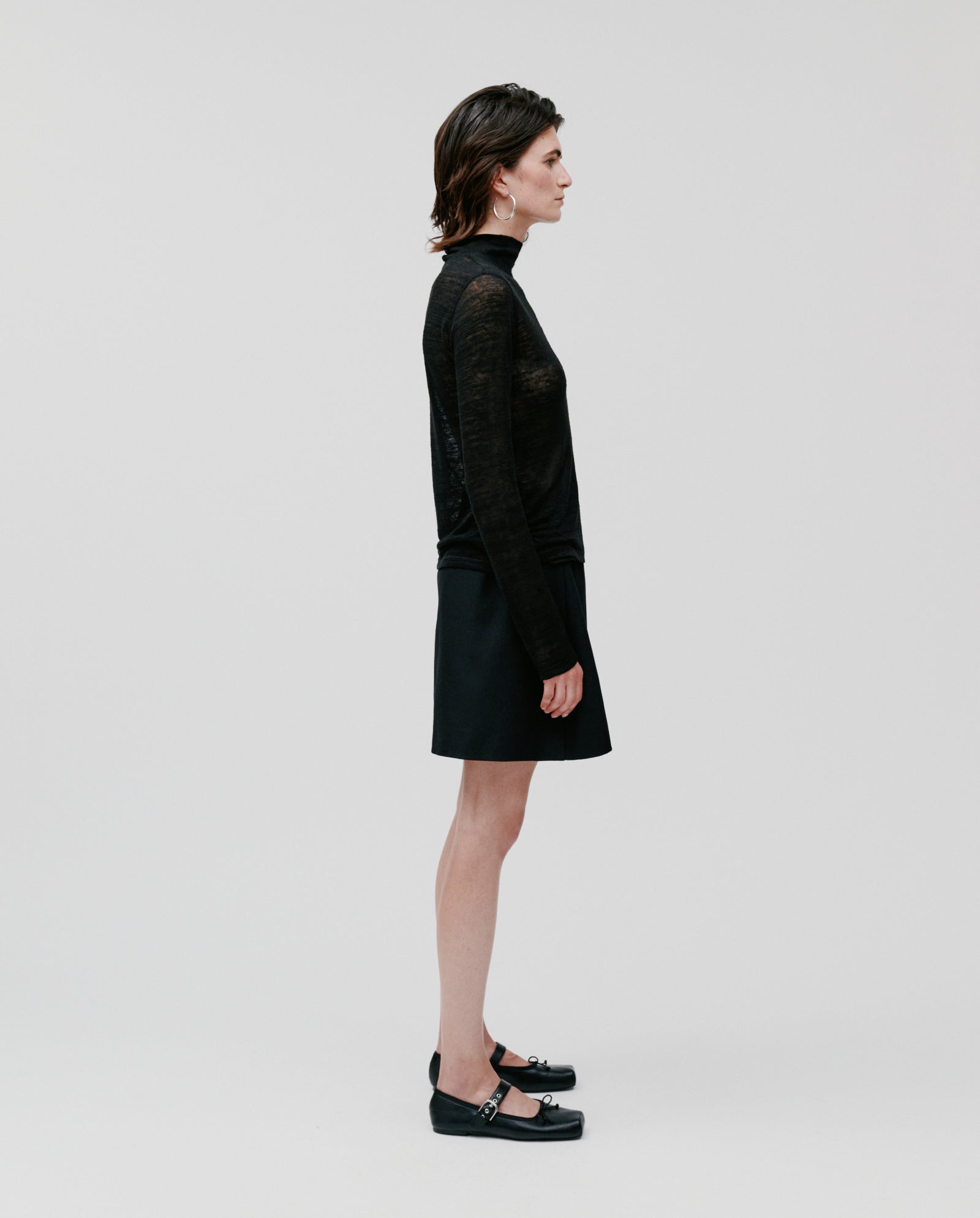 A person stands in profile against a plain background, wearing the IVY OAK FELINE Top paired with a black skirt and black shoes.