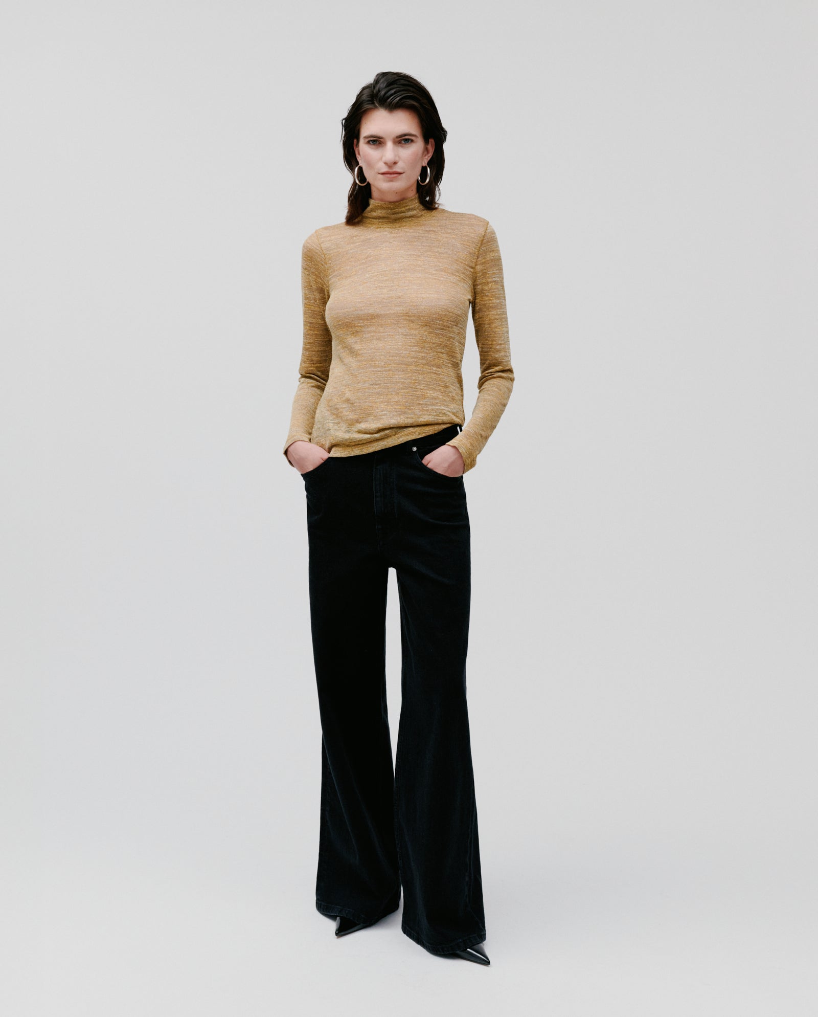 A woman stands with her hands in her pockets, wearing the yellow FELINE Top by IVY OAK and black wide-leg pants.
