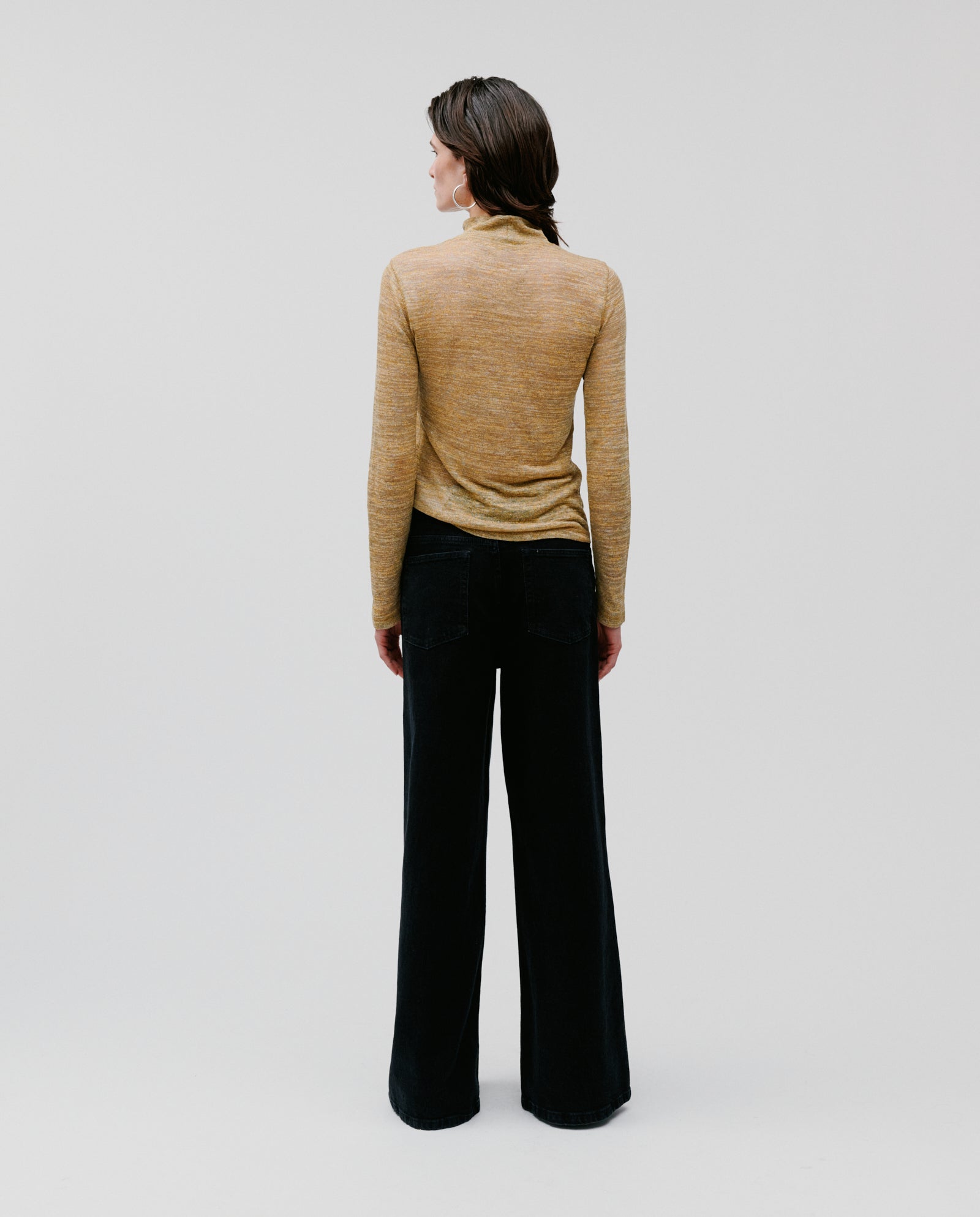 A person stands facing away against a plain background, wearing the FELINE Top by IVY OAK, a tan linen blend rollneck jumper, paired with black wide-leg pants.