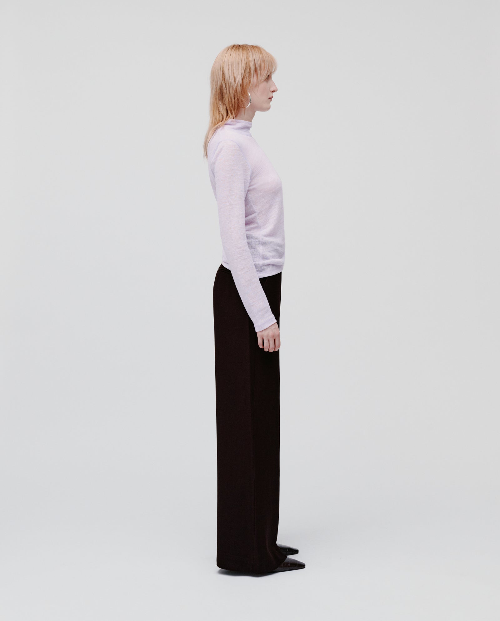 A person with blonde hair stands in profile against a white background, wearing the IVY OAK FELINE Top and black pants.