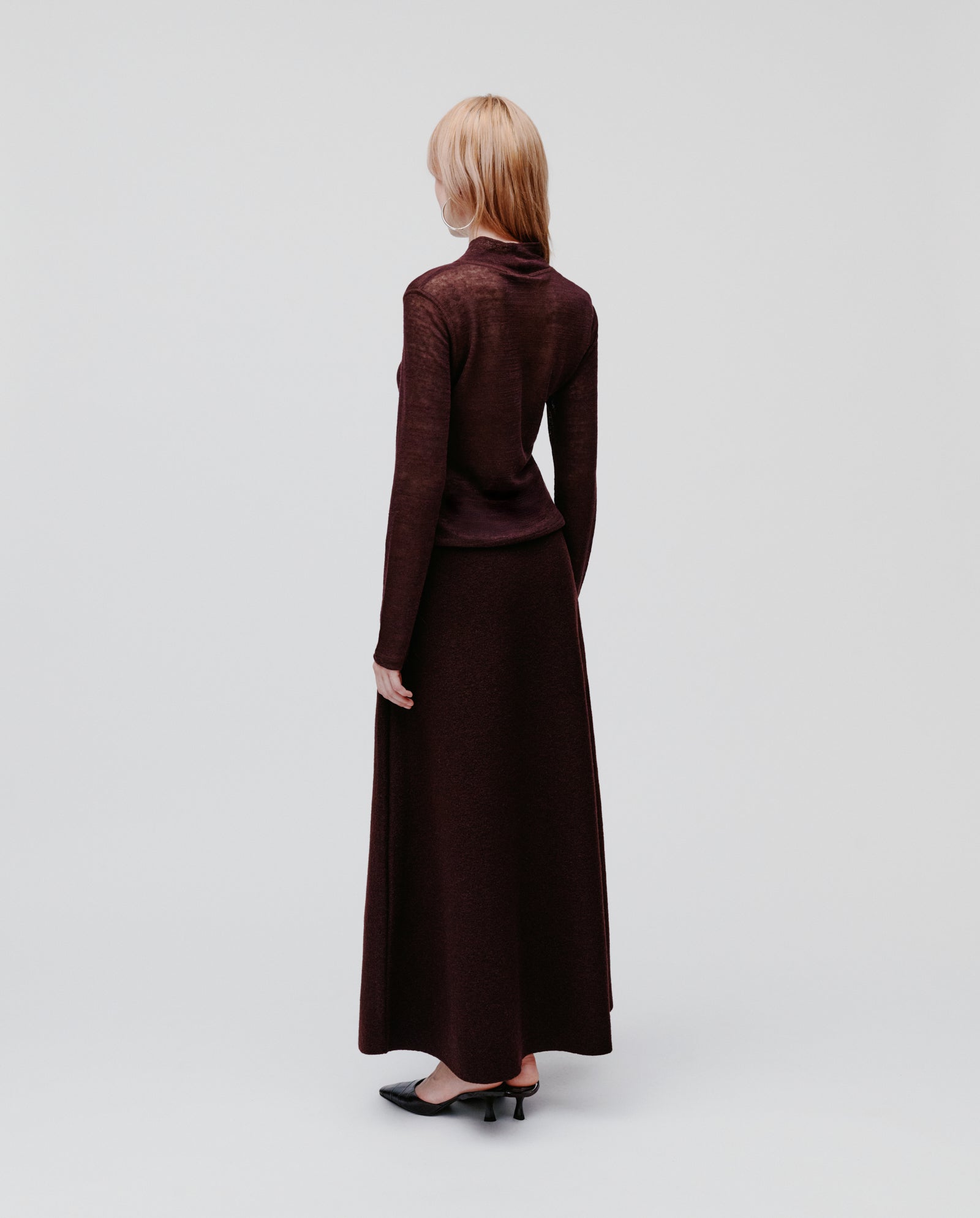 A woman with blonde hair stands facing away, wearing the maroon FELINE Top by IVY OAK with a matching long skirt.