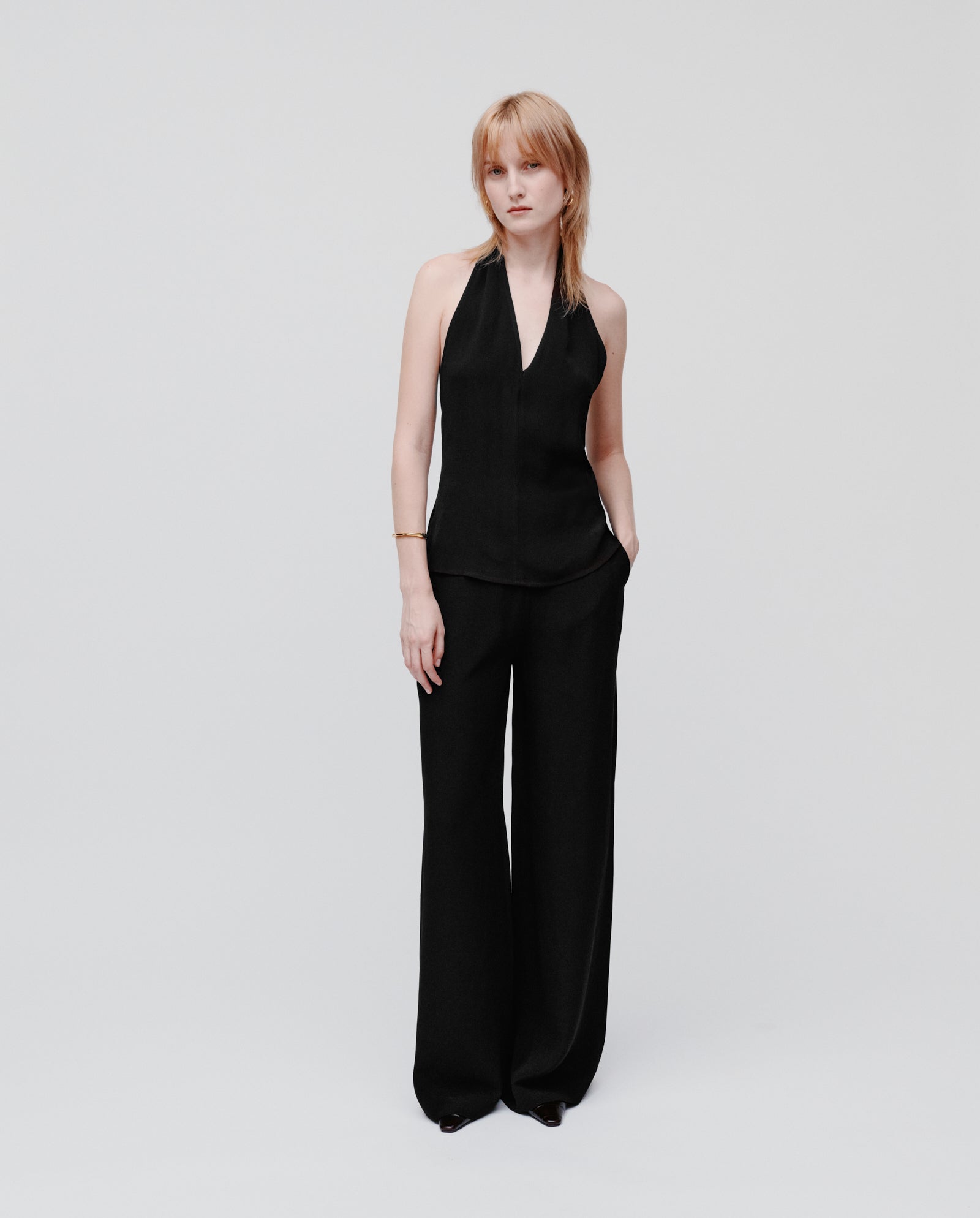A woman wears the IVY OAK TANSY sleeveless black neckholder top with wide-leg black crepe pants, standing against a plain white background.