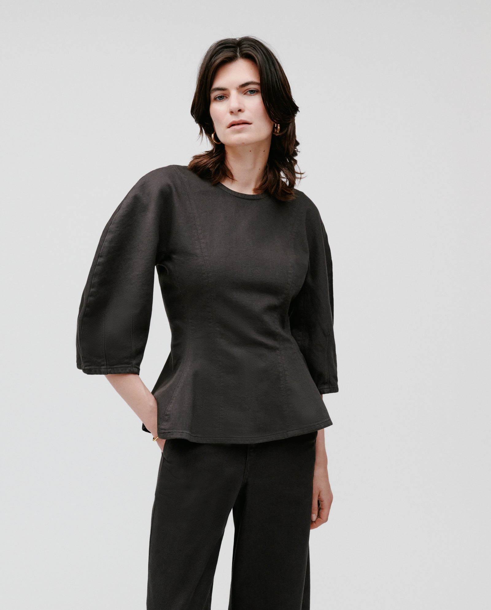 A woman wears the IVY OAK ELMA Blouse, a black three-quarter sleeve top with a subtle peplum style, paired with black pants and posed against a plain white background.