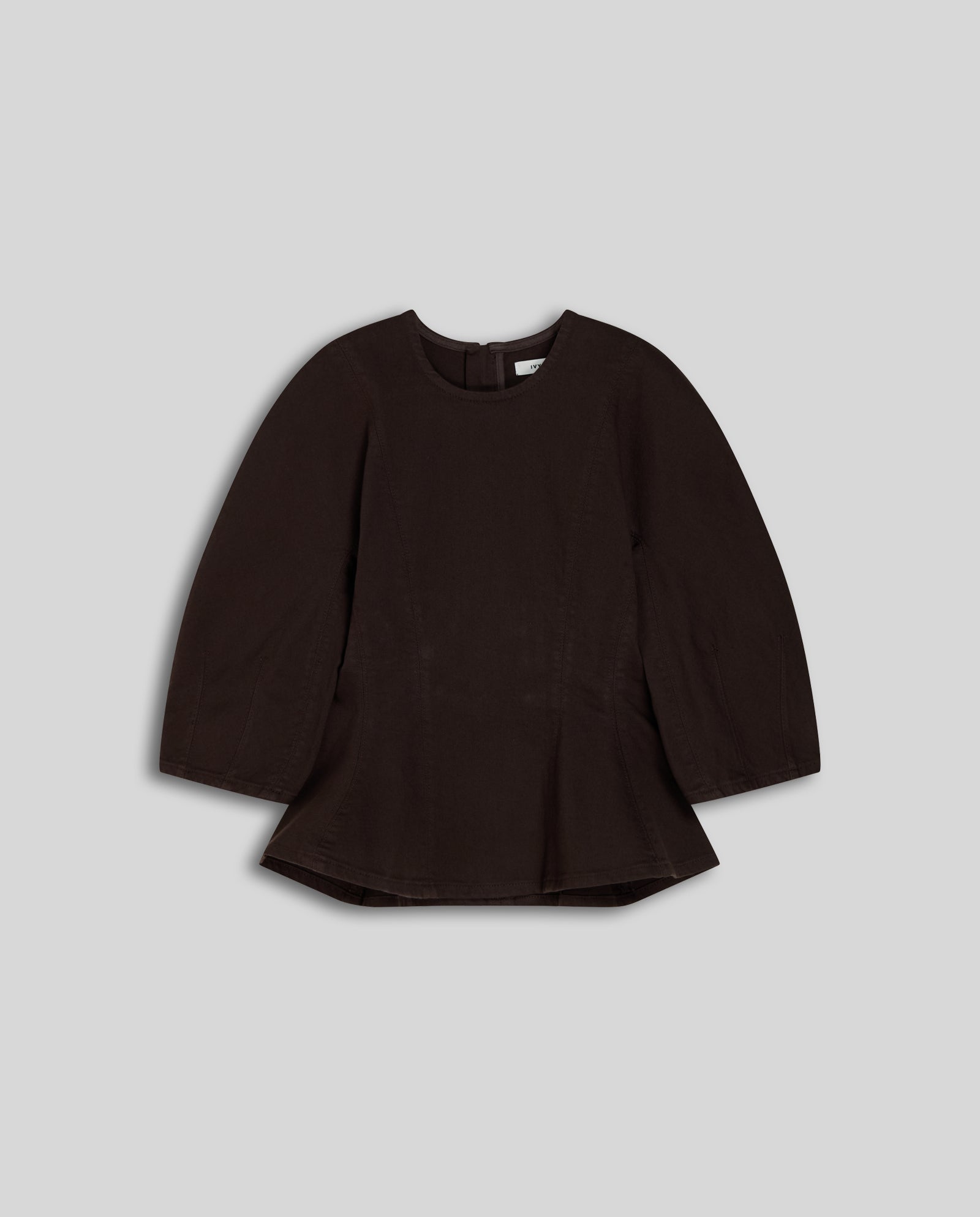 The ELMA Blouse by IVY OAK is a dark brown, long-sleeved top with a round neckline and subtle peplum design, shown against a plain gray background.
