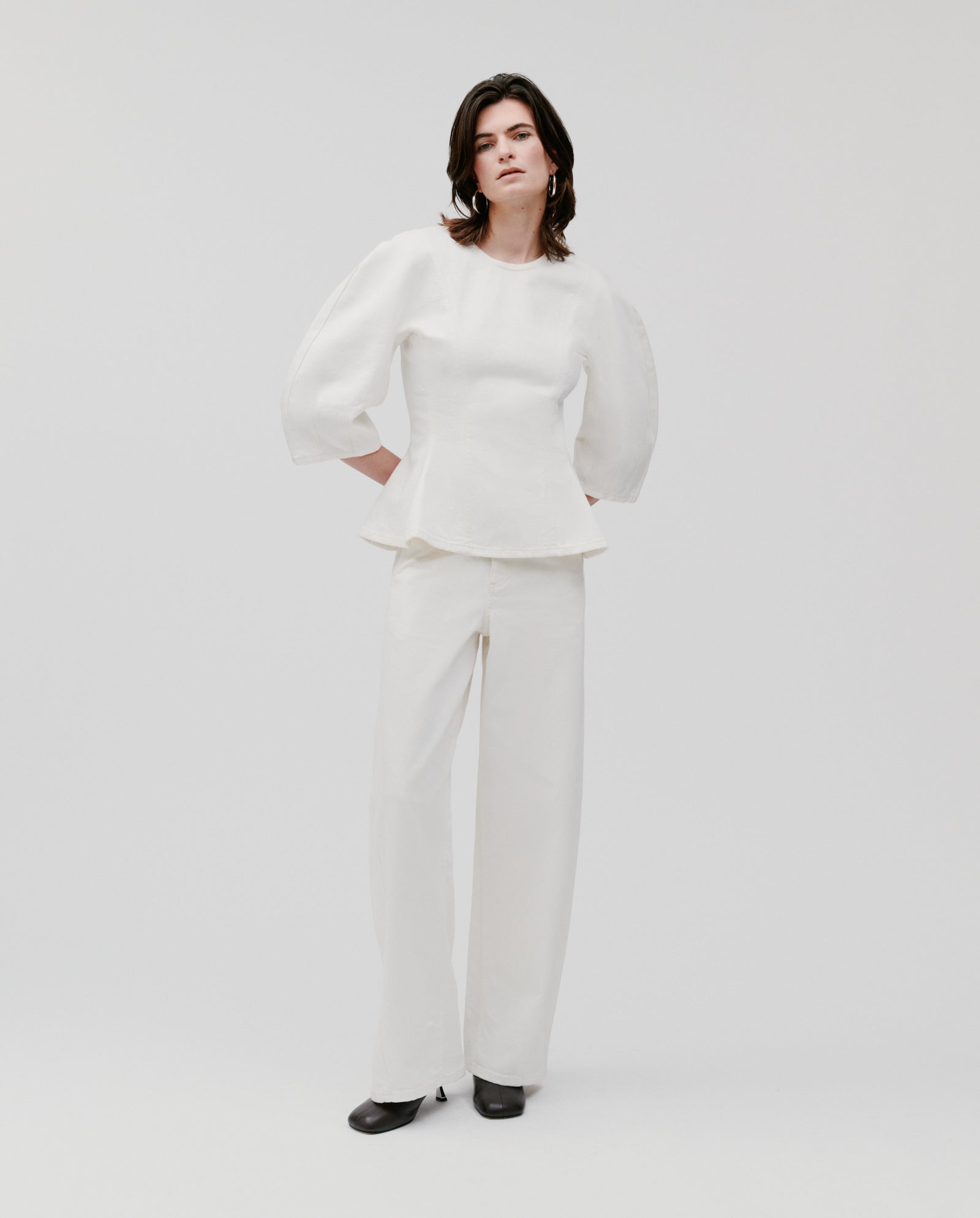 A woman stands against a plain background wearing the IVY OAK ELMA Blouse, featuring wide shoulders and puff sleeves, styled with white wide-leg pants.