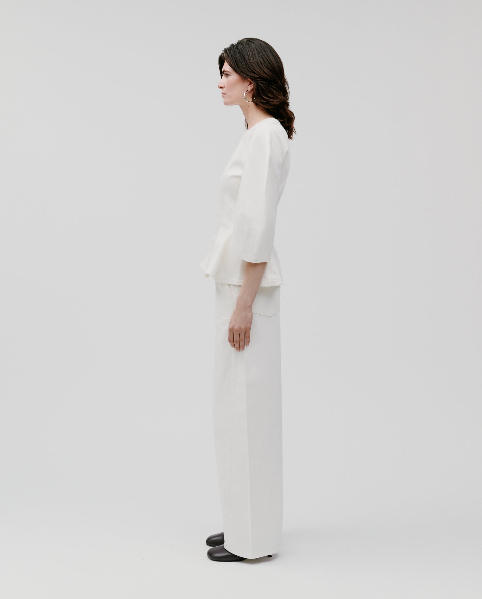 A woman stands in profile against a plain white background, wearing the IVY OAK ELMA Blouse with black shoes.