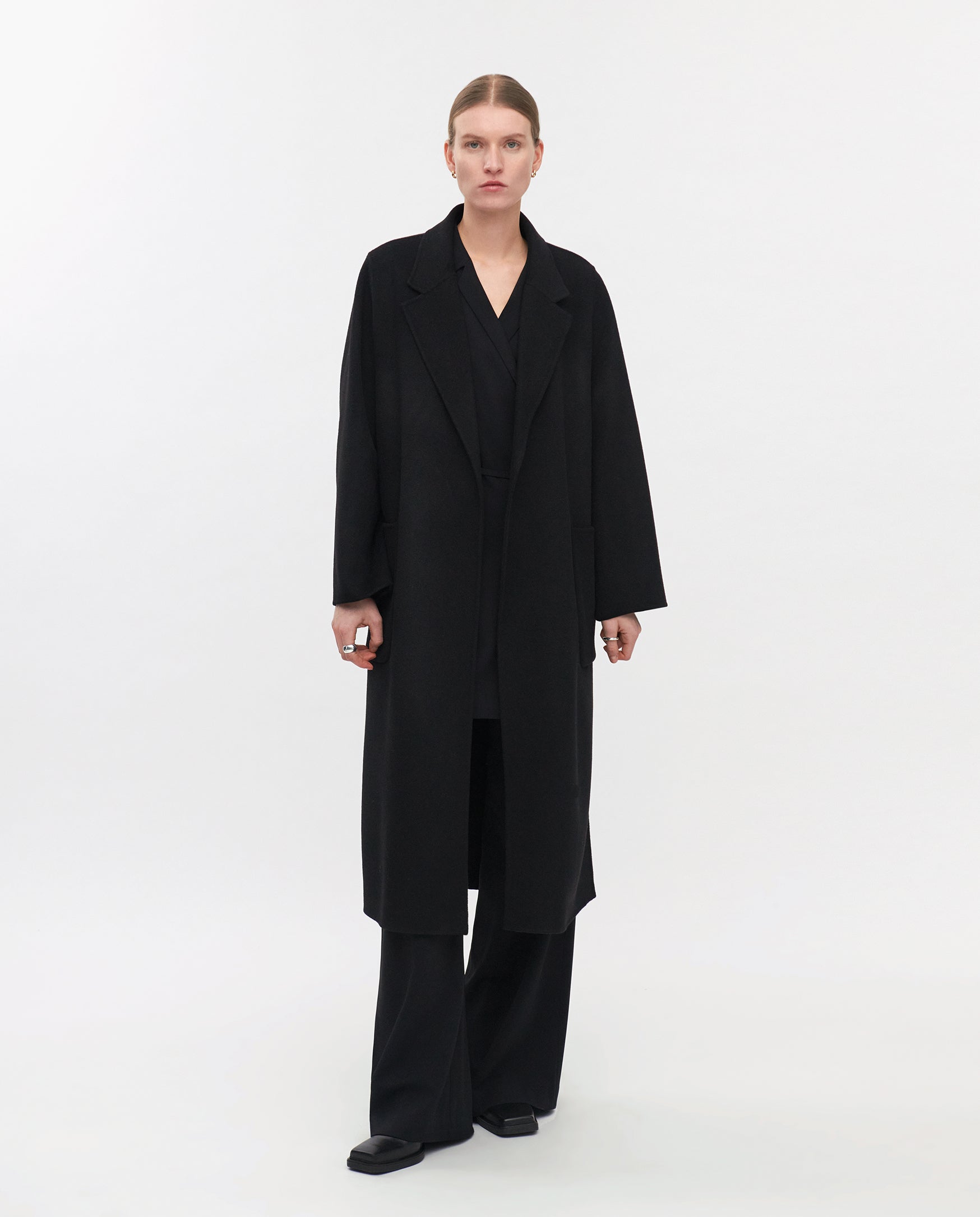 A person stands against a white background wearing the IVY OAK CELIA Doubleface Coat, paired with black trousers and black shoes.