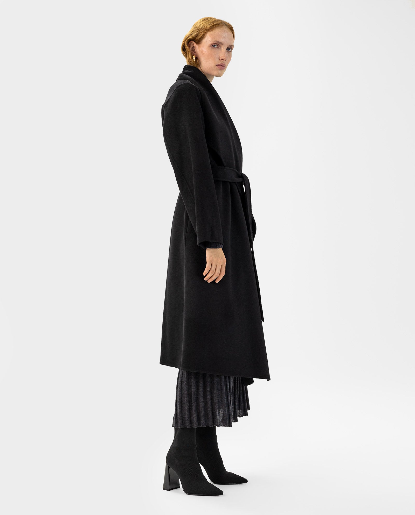 A woman wears the IVY OAK CARRIE ROSE Wool Coat with a pleated skirt and heeled boots, standing against a plain white background.