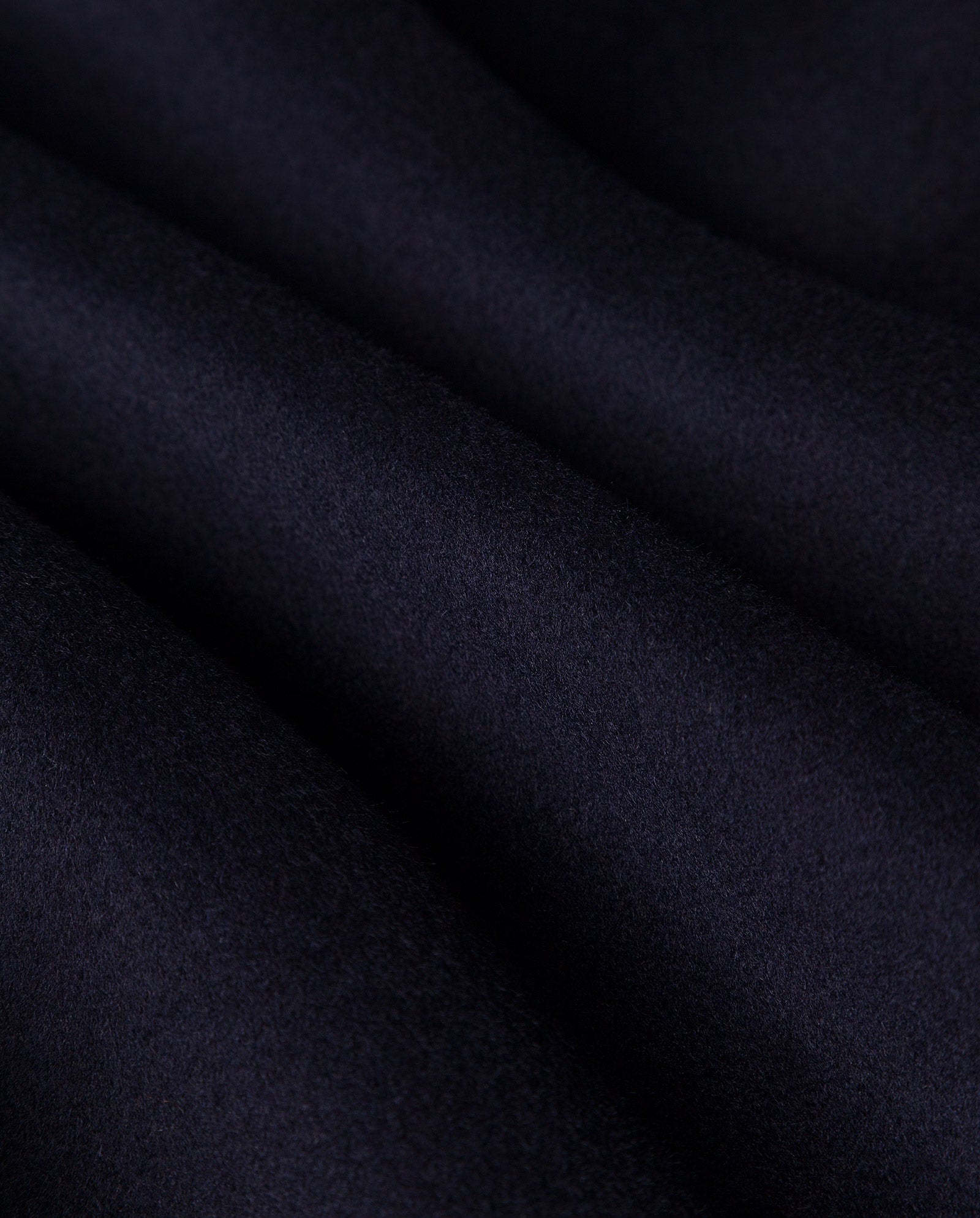 Close-up of dark, soft fabric with gentle folds, showing the smooth, velvety texture of the CARRIE ROSE Wool Coat by IVY OAK, crafted from Responsible Wool Standard certified material.
