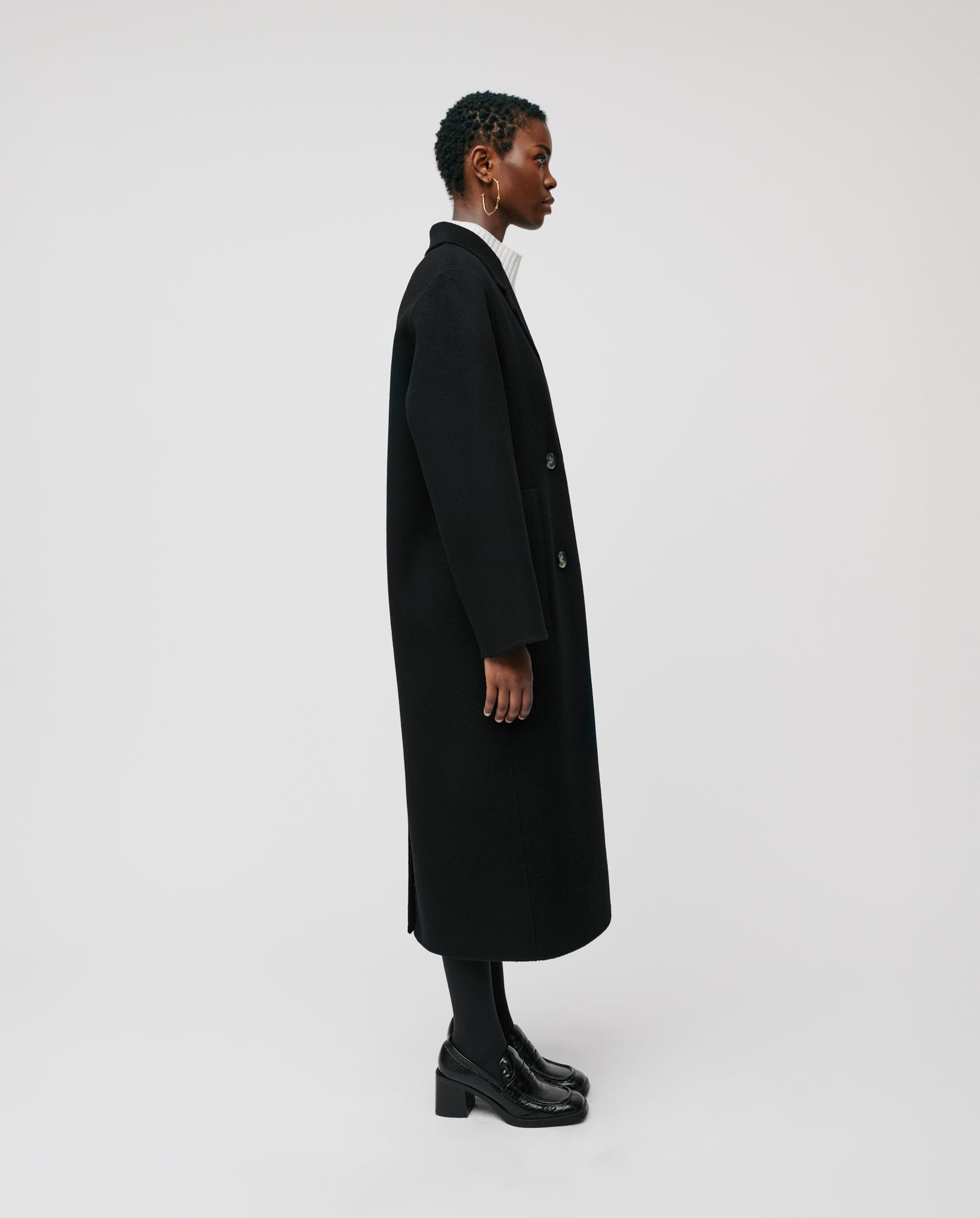 A person wearing the IVY OAK CLARA Wool Coat in an oversized fit, made with Responsible Wool Standard material, paired with black shoes, stands in profile against a plain white background.