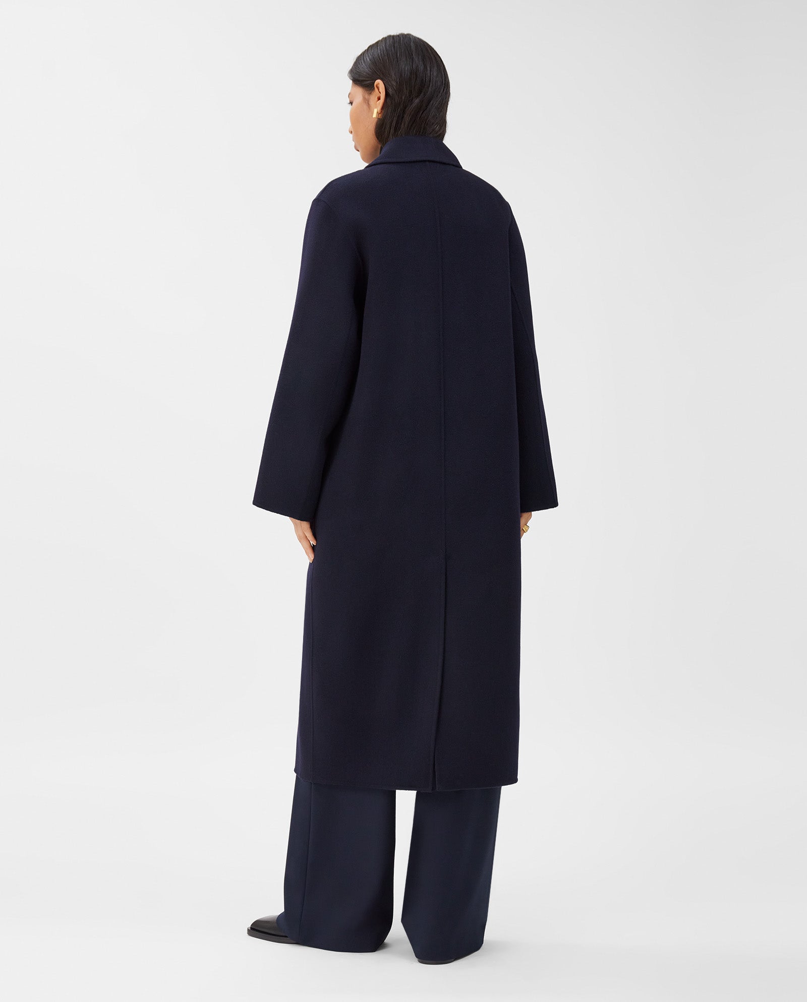 A person stands with their back to the camera, wearing the IVY OAK CLARA Wool Coat in an oversized, long dark midi style and dark pants against a plain background.