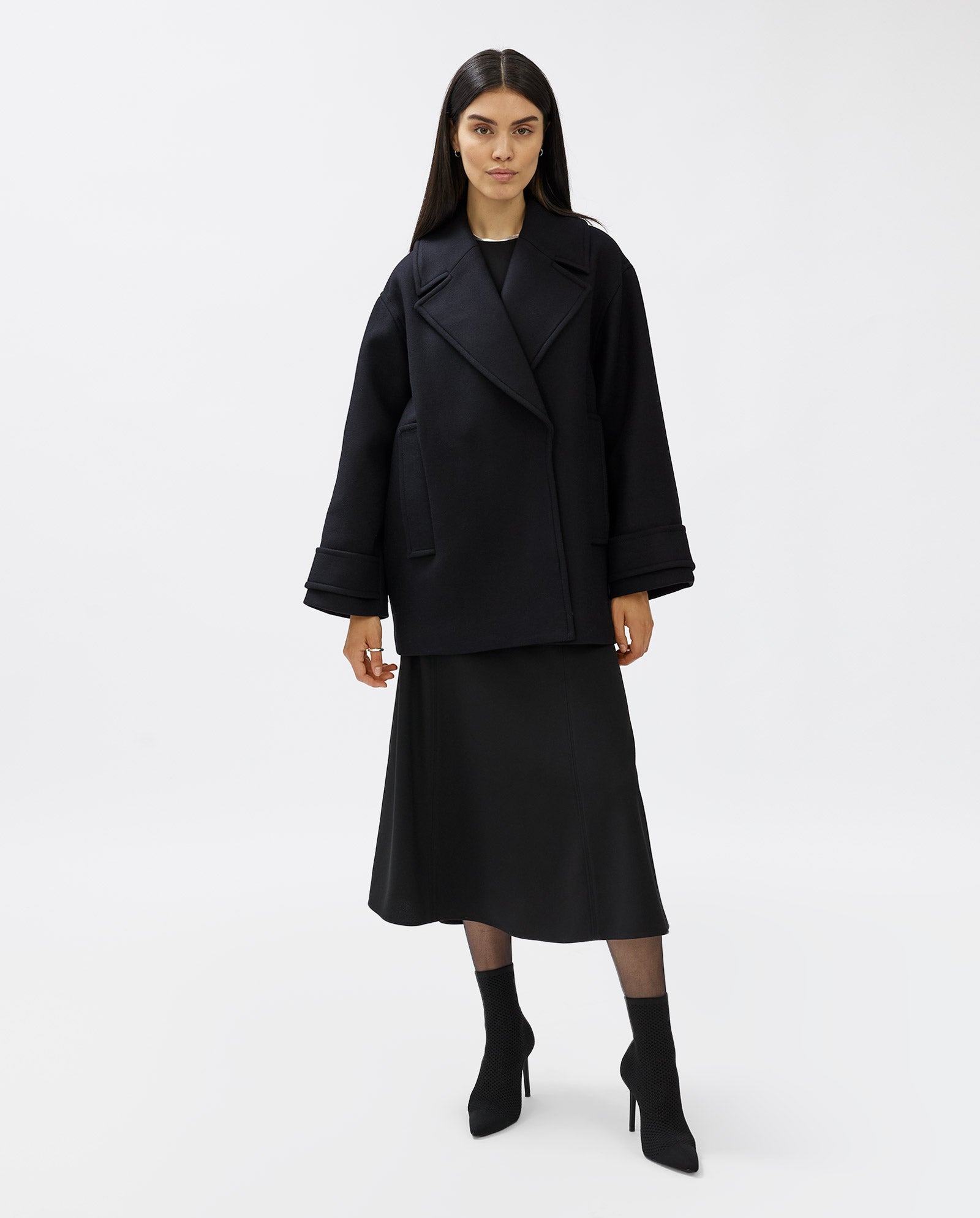 A woman wearing the IVY OAK CARLY Coat, styled with a black midi skirt and black heeled boots, stands against a white background.