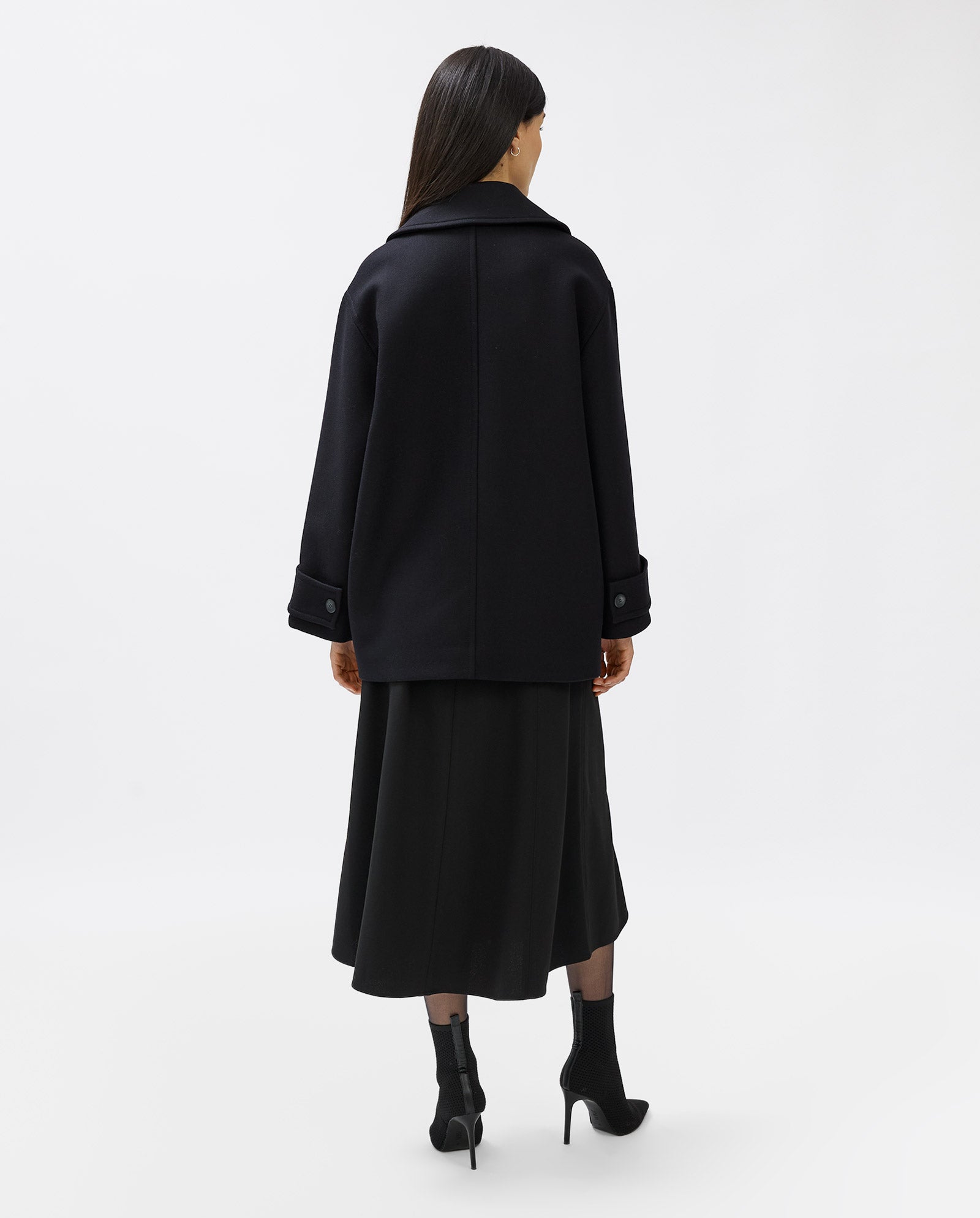 A woman in the IVY OAK CARLY Coat, styled with a skirt and boots, stands facing away against a plain white background.