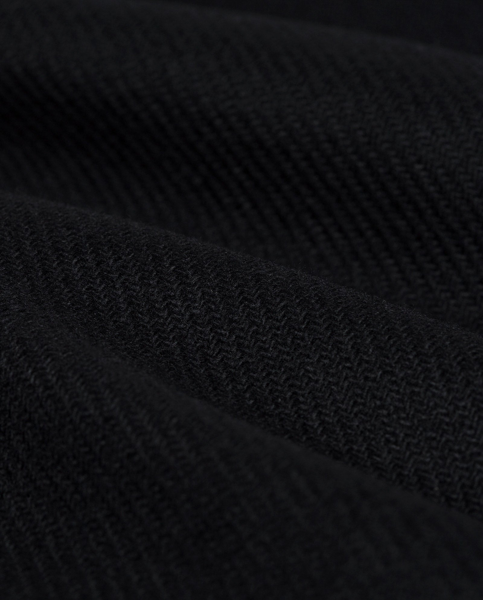 Close-up of the black herringbone-textured fabric with soft, wavy folds from the CARLY Coat by IVY OAK, featuring an oversized fit and a hidden button placket.