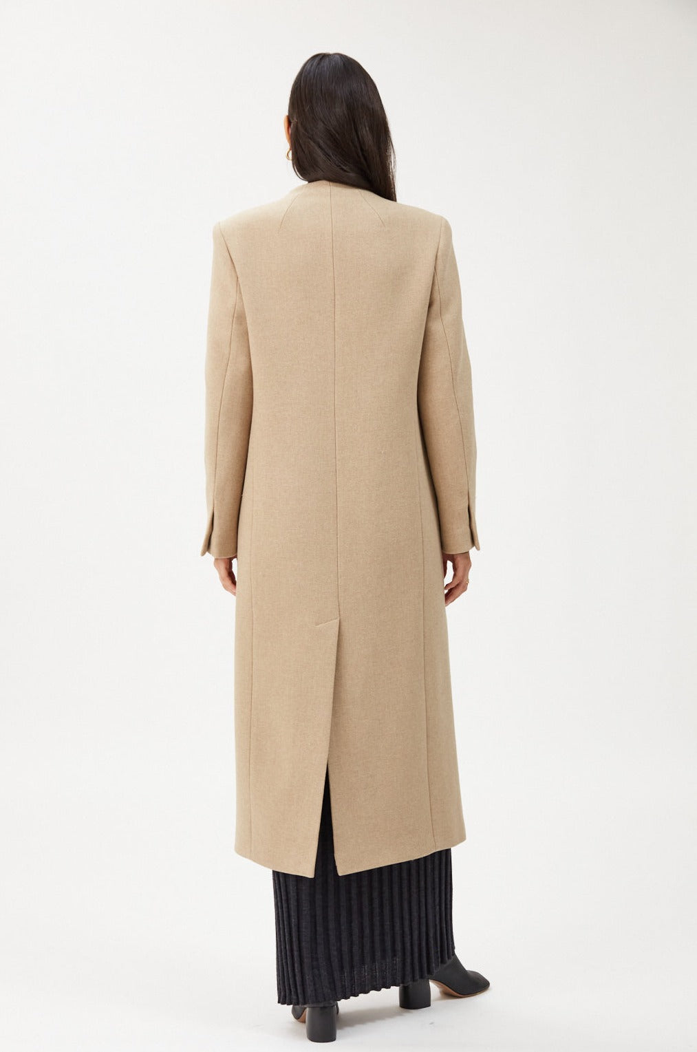 A person with long dark hair is seen from the back wearing the IVY OAK CAPRI Coat, a beige wool coat with a stand-up collar, paired with a black skirt against a white background.