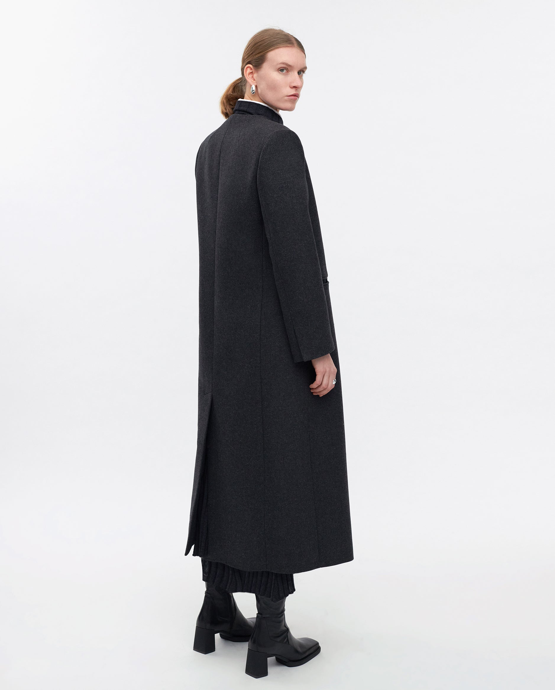 Woman wearing the IVY OAK CAPRI Coat in a maxi length, paired with black boots and earrings, standing sideways against a plain white background.
