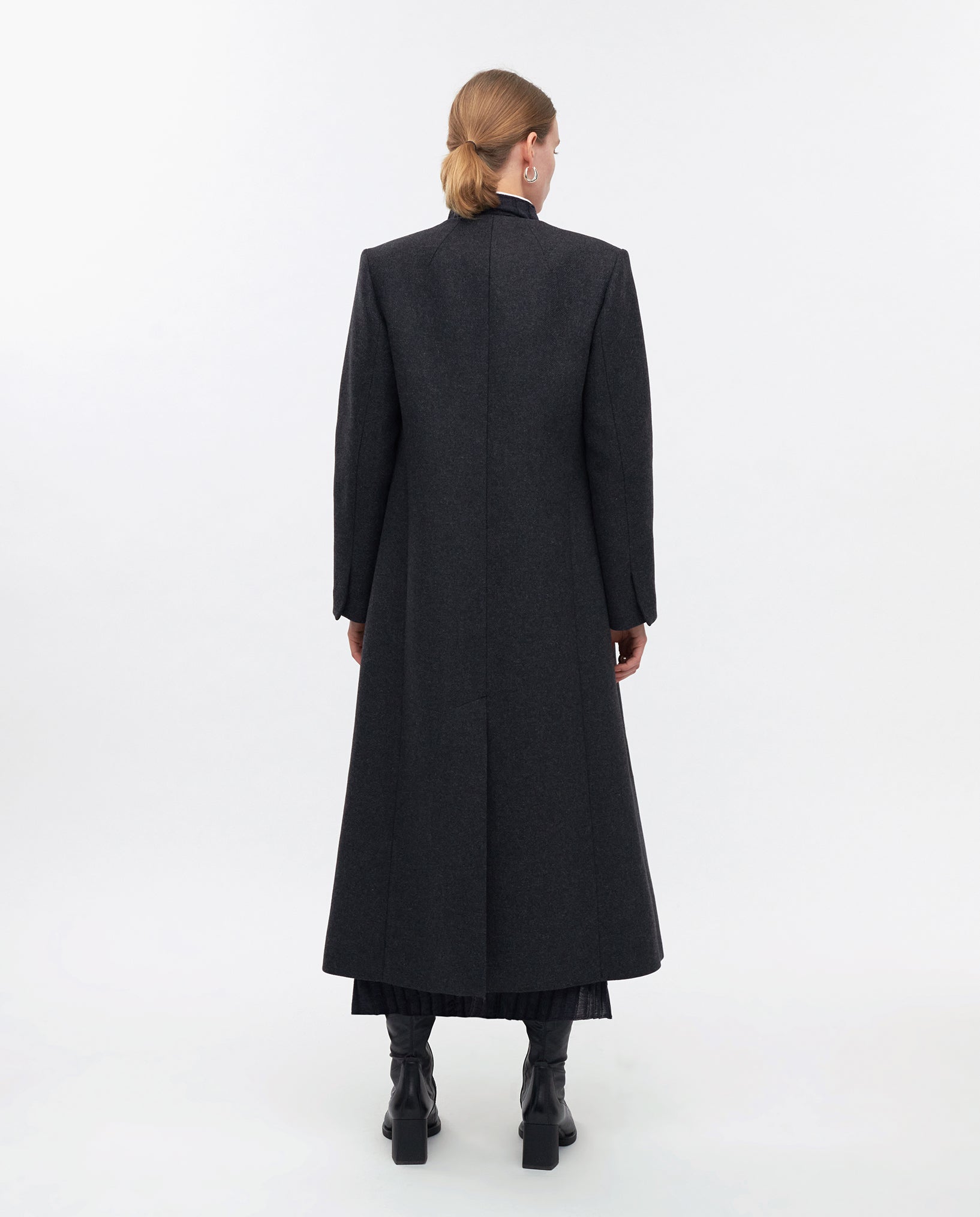 A woman facing away, wearing the maxi-length IVY OAK CAPRI Coat and black boots, showcases sleek MWOOL® Styles against a plain white background.
