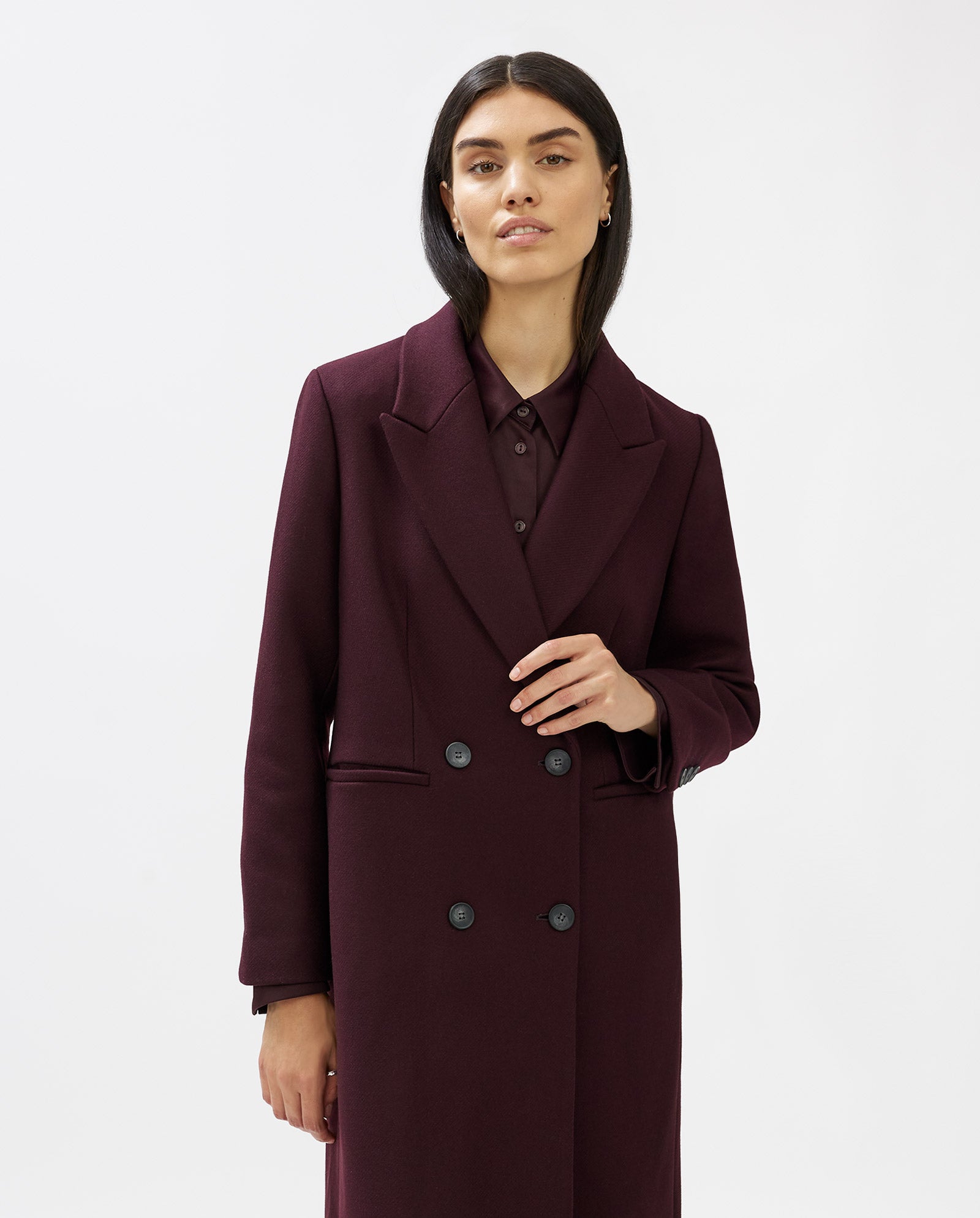 A woman wears the IVY OAK CAYENNE coat, a long, dark burgundy knee-length piece with a loose fit, layered over a matching shirt and posed against a white background.