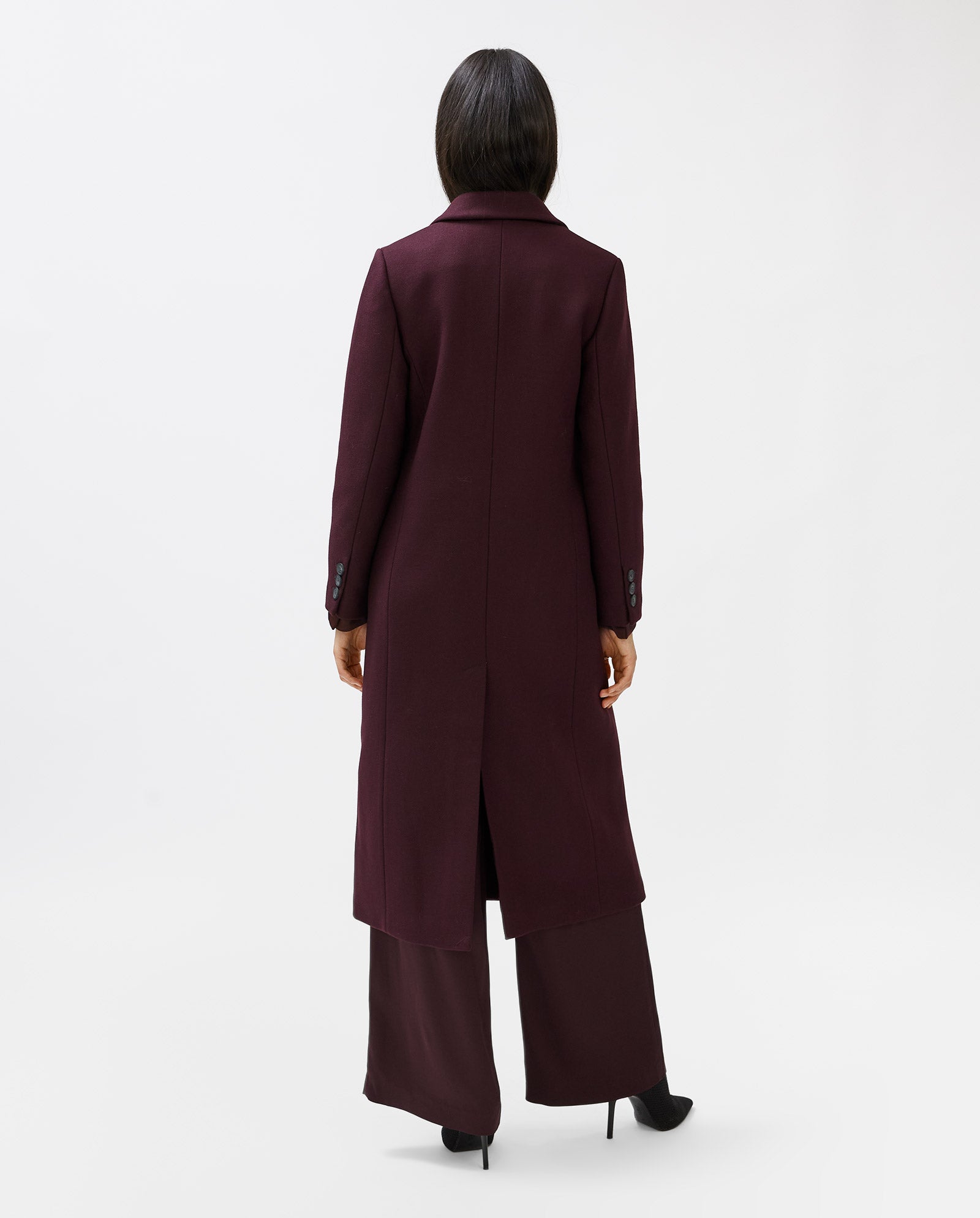 A person stands with their back to the camera, wearing the IVY OAK CAYENNE knee-length wool coat in burgundy and wide-leg pants.