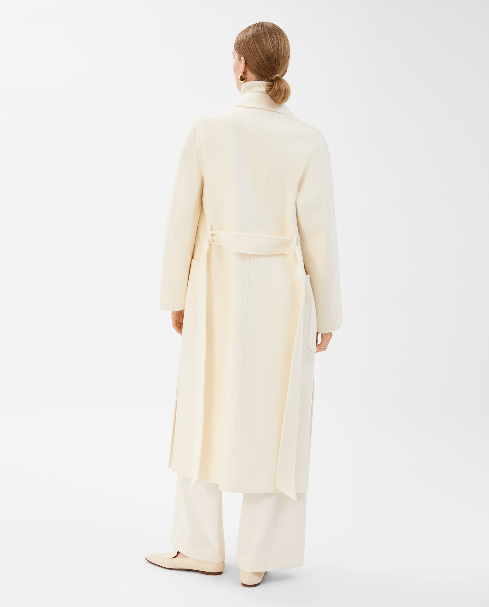 Woman wearing the IVY OAK CELIA Doubleface Wool Coat, a loose fit, cream-colored wool design paired with wide-leg pants, standing and facing away on a white background.