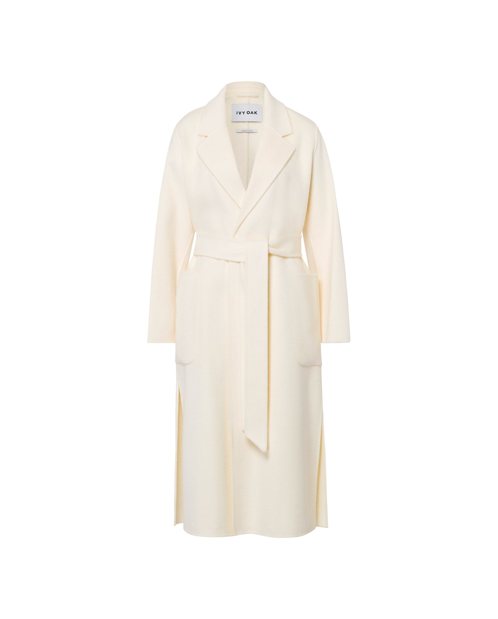 The CELIA Doubleface Wool Coat by IVY OAK is a cream-colored, loose-fit wool coat with a midi length, belted waist, lapels, and large front pockets, shown on a white background.