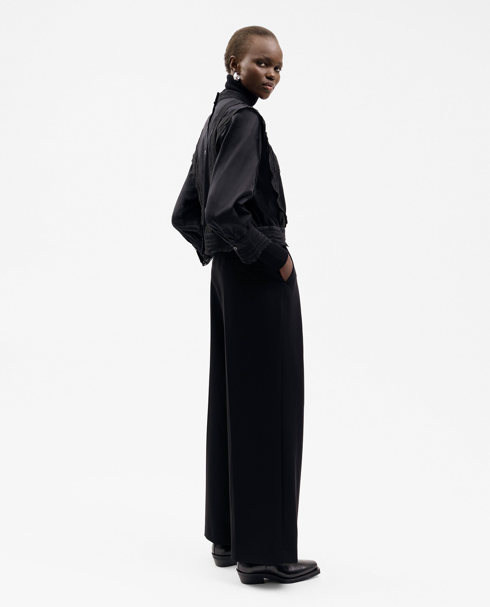 Wearing the IVY OAK ELINOR Blouse, a person stands sideways in black wide-leg pants and a black cropped top against a plain white background.