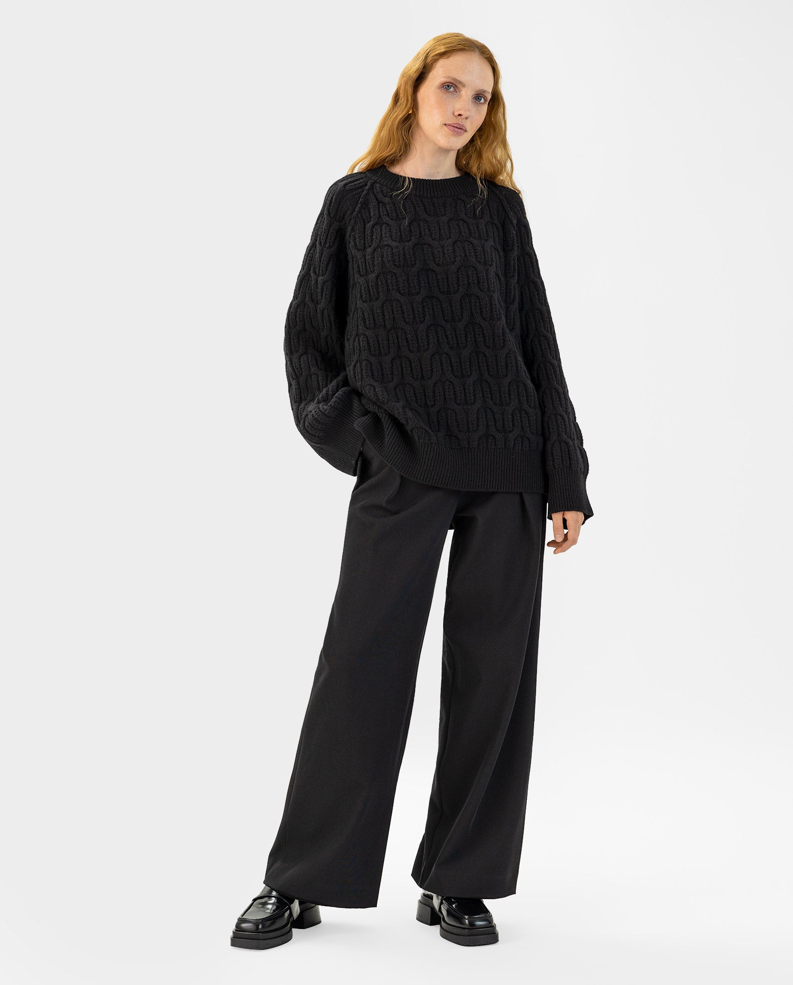 Wearing the IVY OAK KLARINA Jumper in black extrafine merino wool and loose black pants with black shoes, a person stands against a white background.