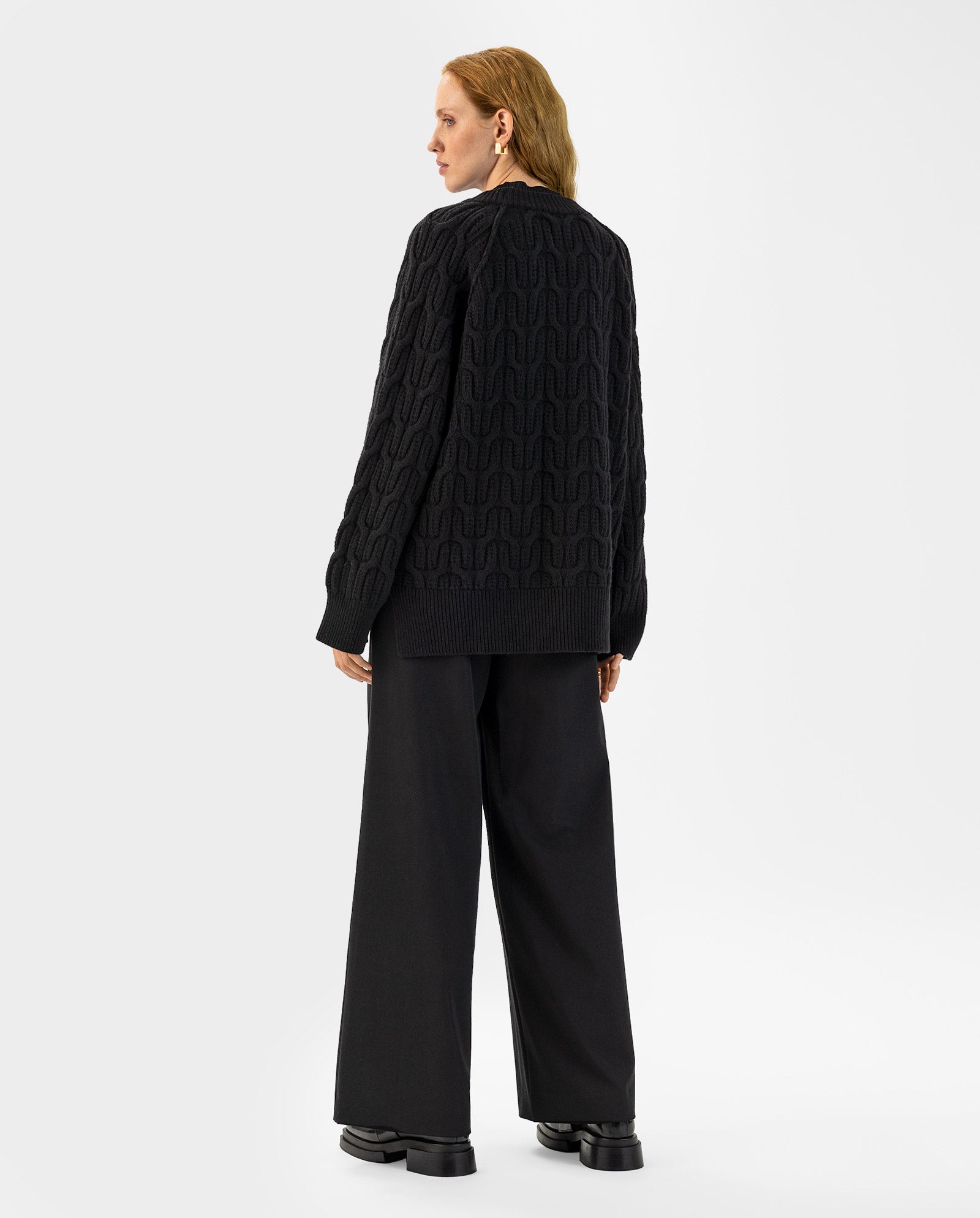 A person stands facing away, wearing the IVY OAK KLARINA Jumper in black extrafine merino wool paired with wide, loose-fit black pants.