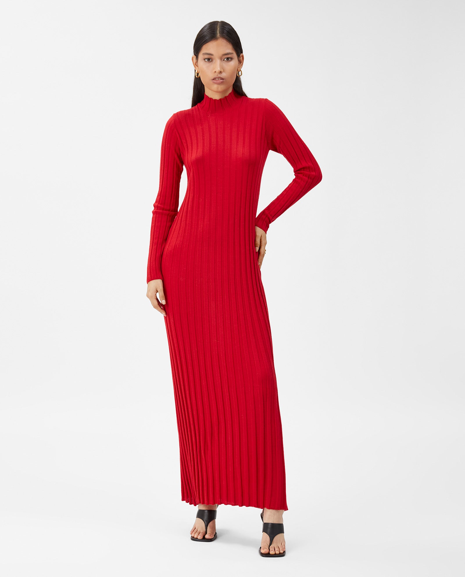 Woman in the IVY OAK KAMELIA Dress— a long-sleeved, red maxi made from extra-fine merino wool—paired with black heeled sandals, stands against a white background.