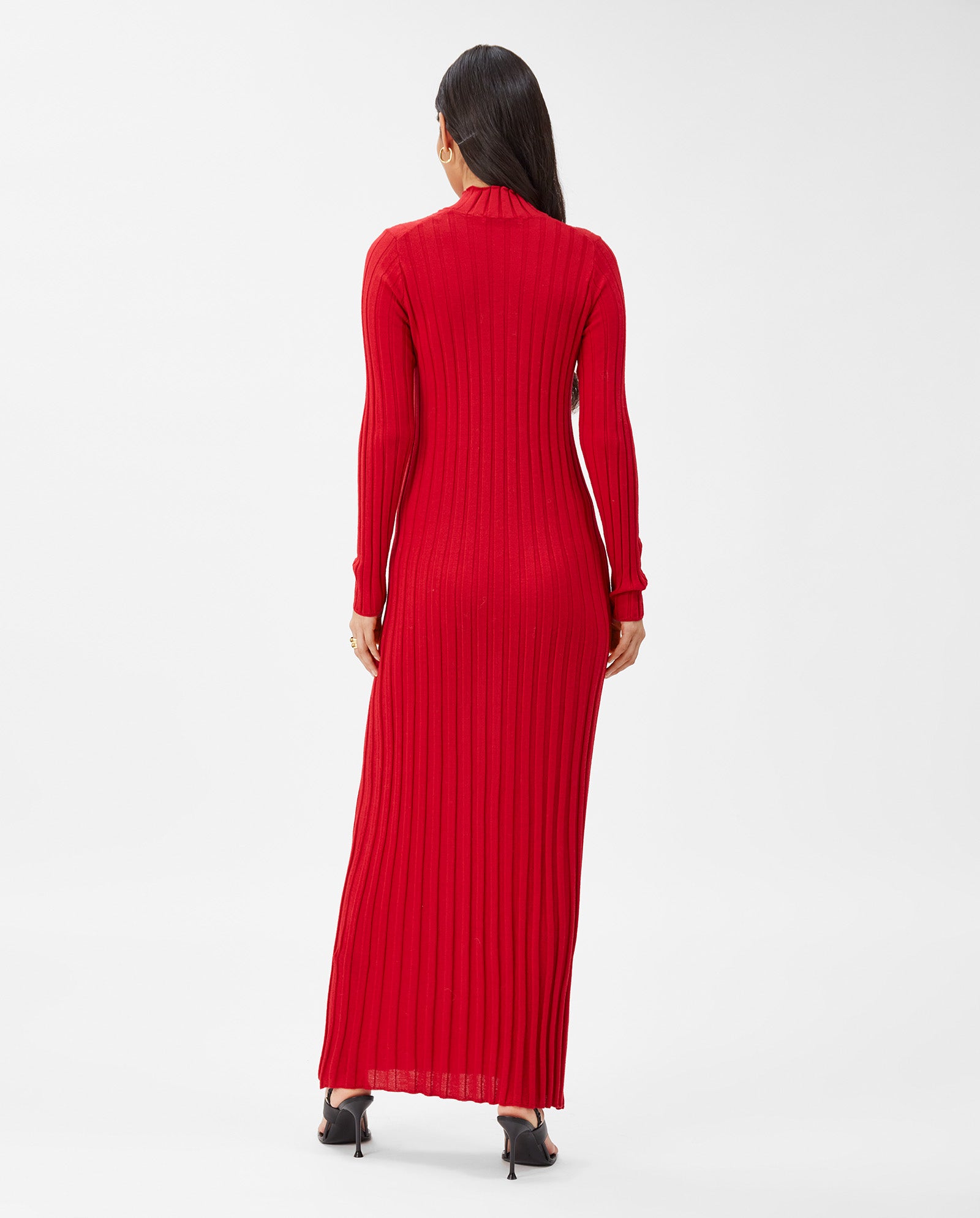 Woman in the IVY OAK KAMELIA Dress—a maxi-length, long-sleeved red gown made from extra-fine merino wool—and black heels stands with her back to the camera.