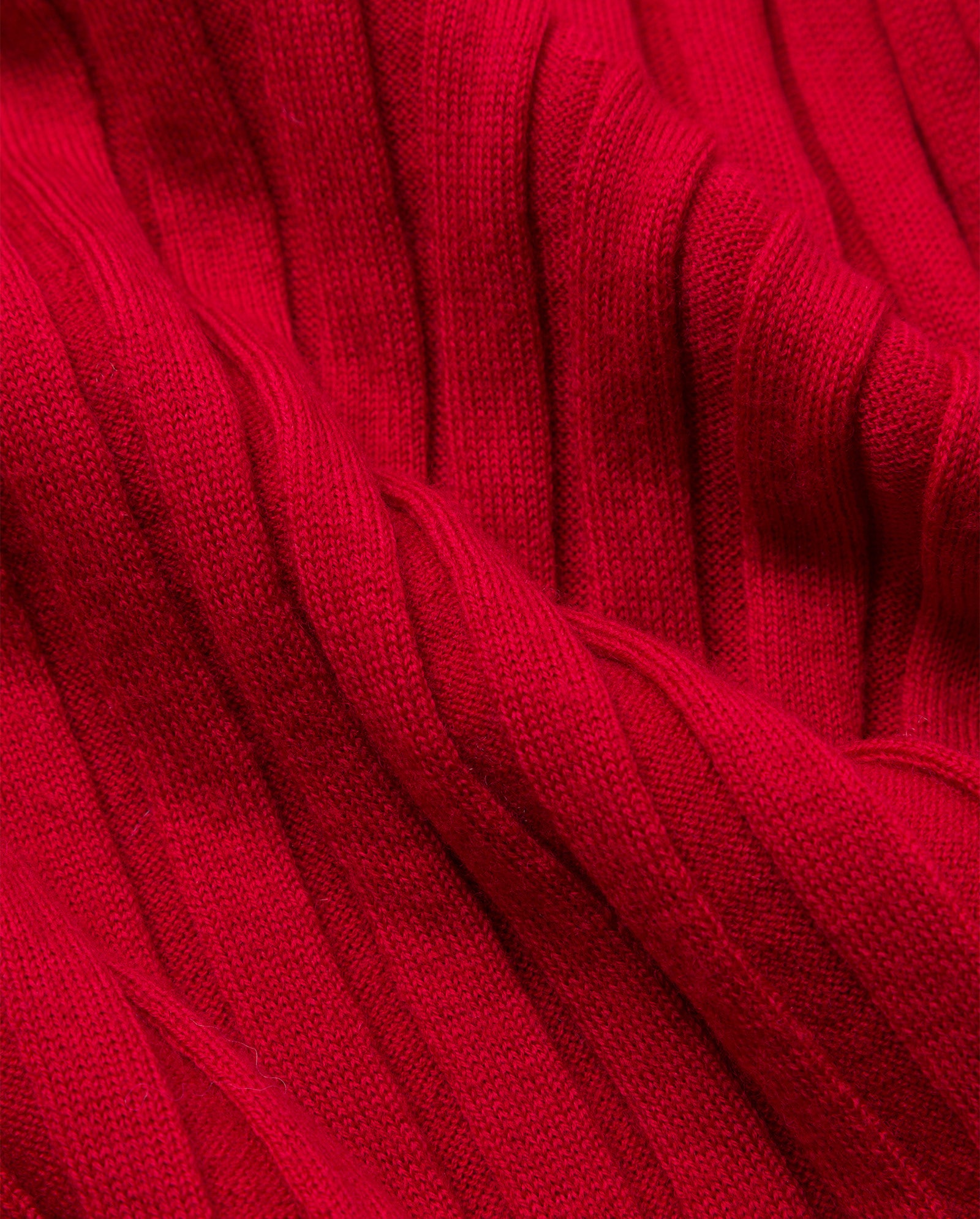 Close-up of ribbed red fabric with a soft, textured surface and vertical knitting, crafted from extra-fine merino wool—featured in the KAMELIA Dress by IVY OAK, perfect for a cozy and stylish look.