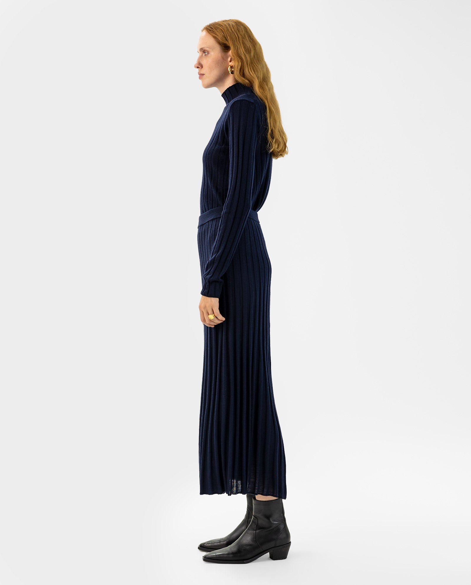 Woman in profile wearing the IVY OAK KALI Skirt, paired with a navy blue, long-sleeve merino wool ribbed knit dress and black ankle boots.