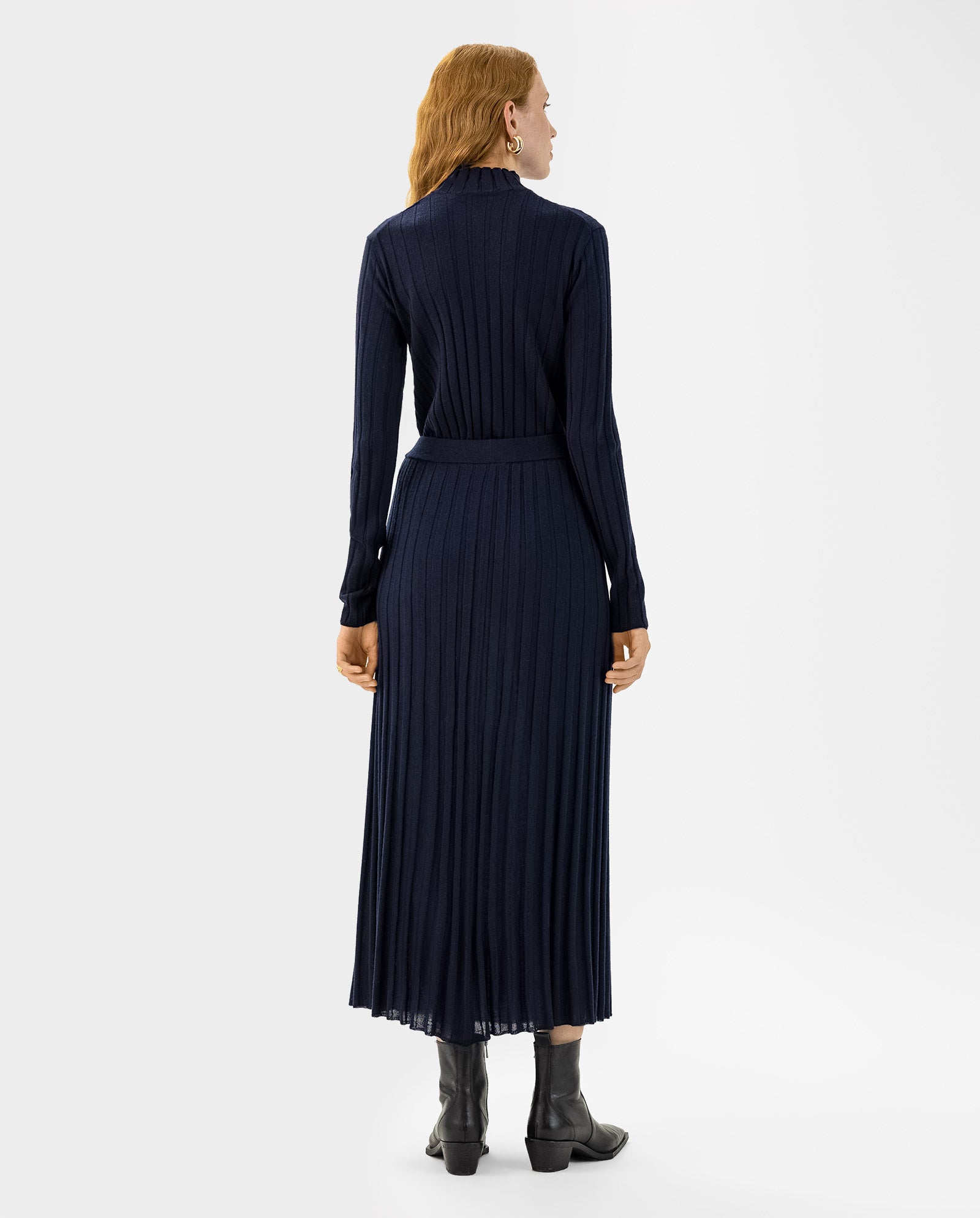 A woman stands with her back to the camera, wearing the IVY OAK KALI Skirt paired with a long-sleeved navy blue ribbed dress and black ankle boots.