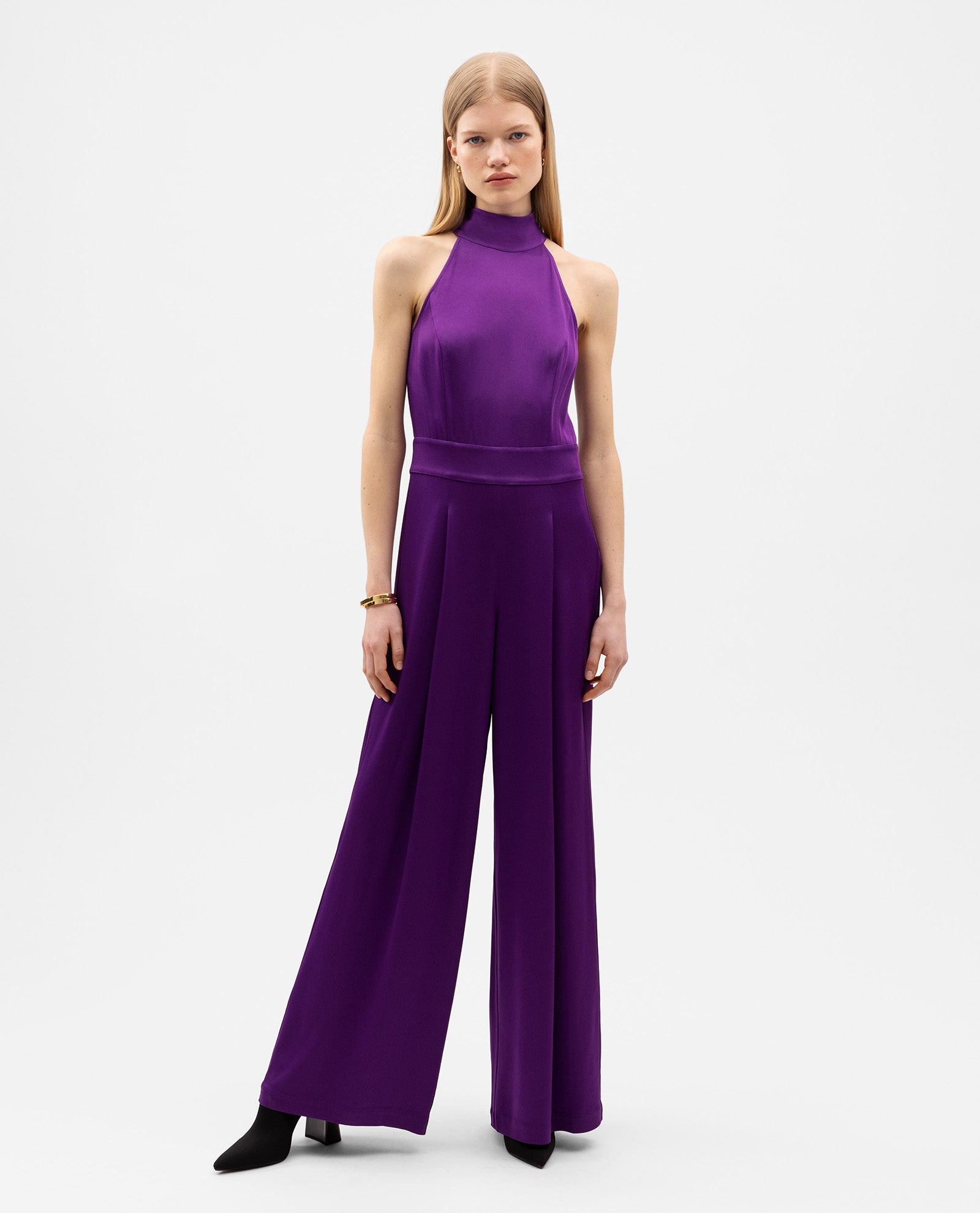 A woman wears the IVY OAK PHILIPPINE Jumpsuit—a sleeveless purple satin piece with a stand collar and wide legs—standing against a white background.
